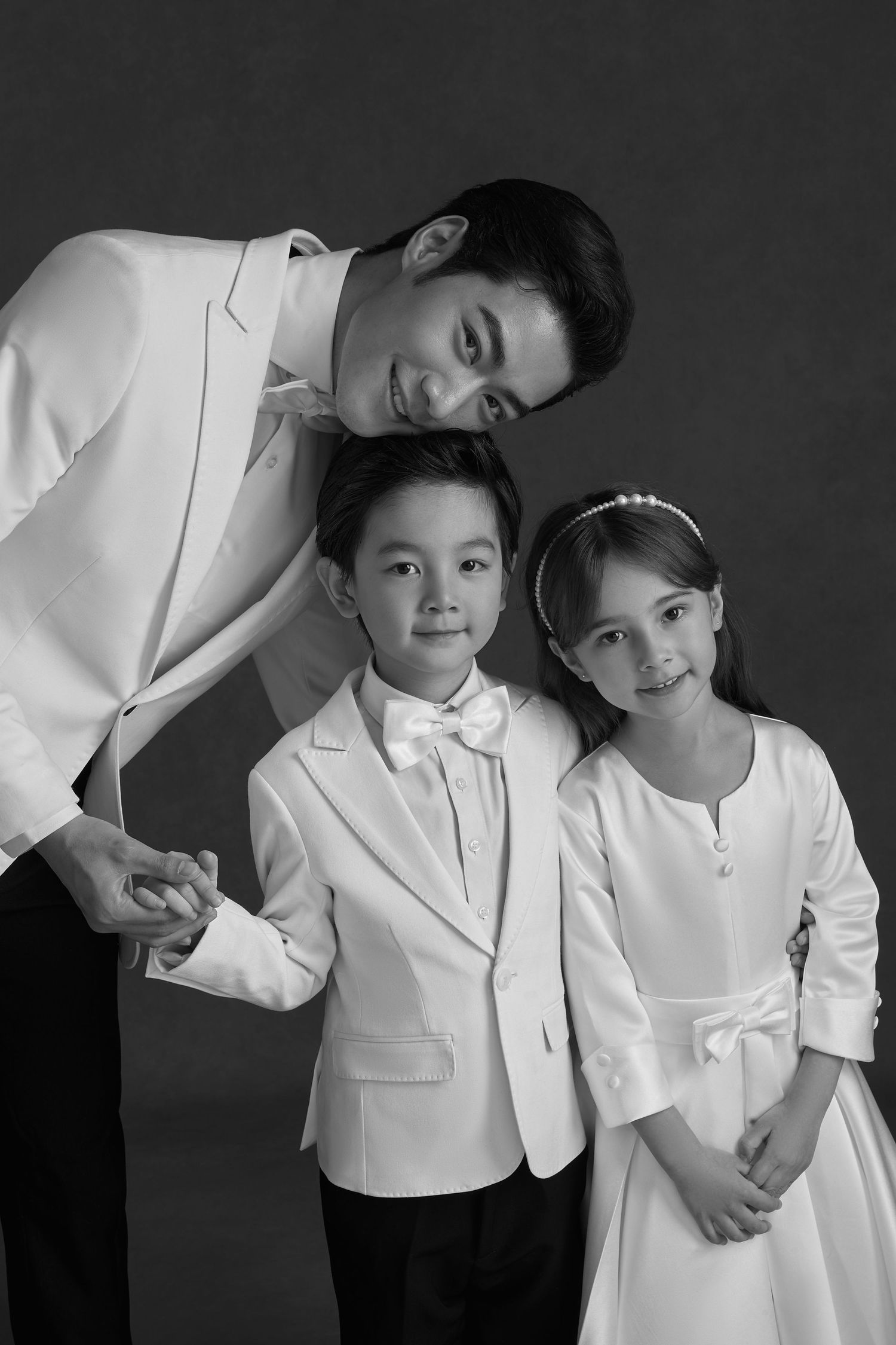 Black and white photo of a father in white suit posing with two children in formal white outfits.