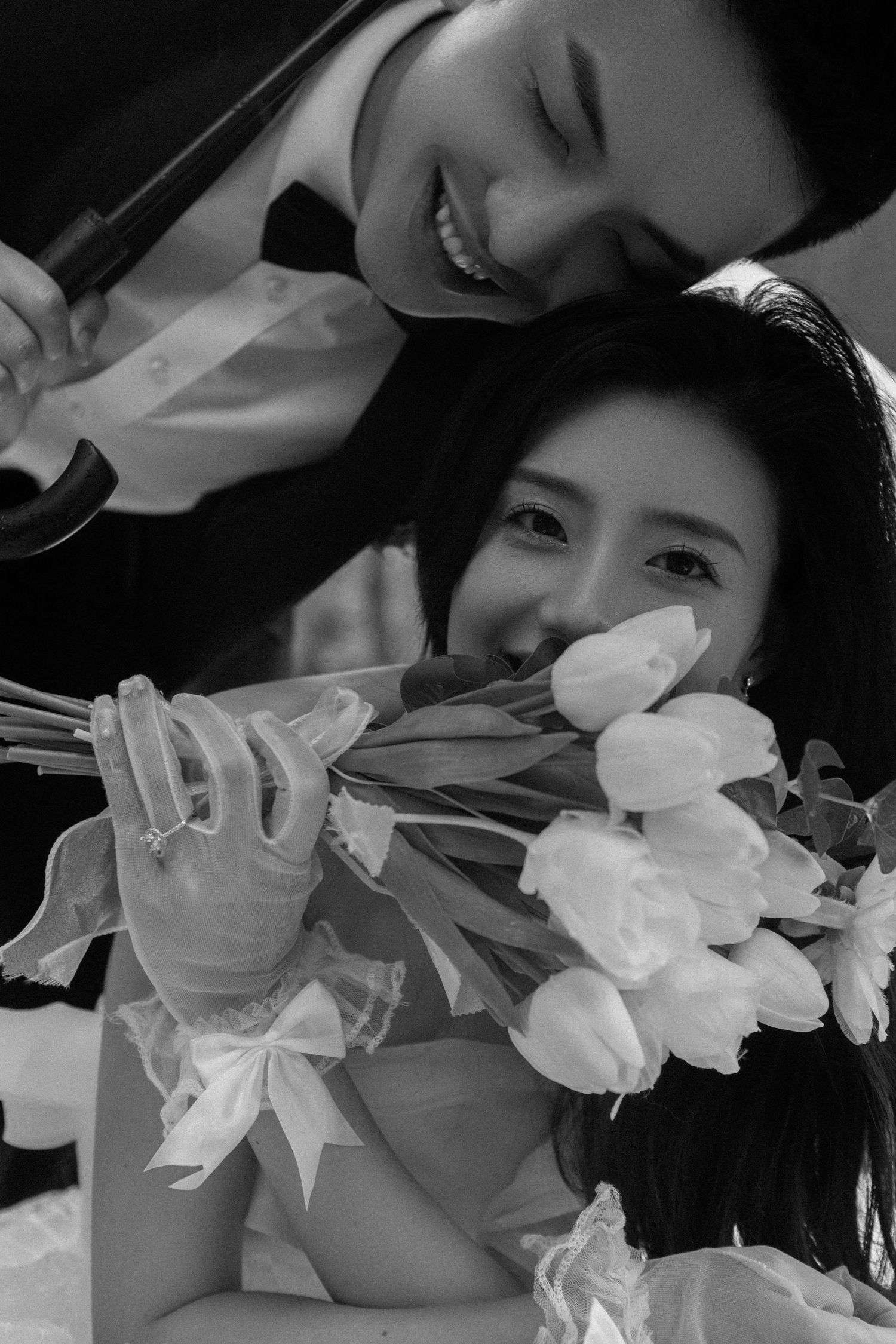 Black and white wedding photo of a smiling bride holding white tulips with groom leaning over her affectionately.