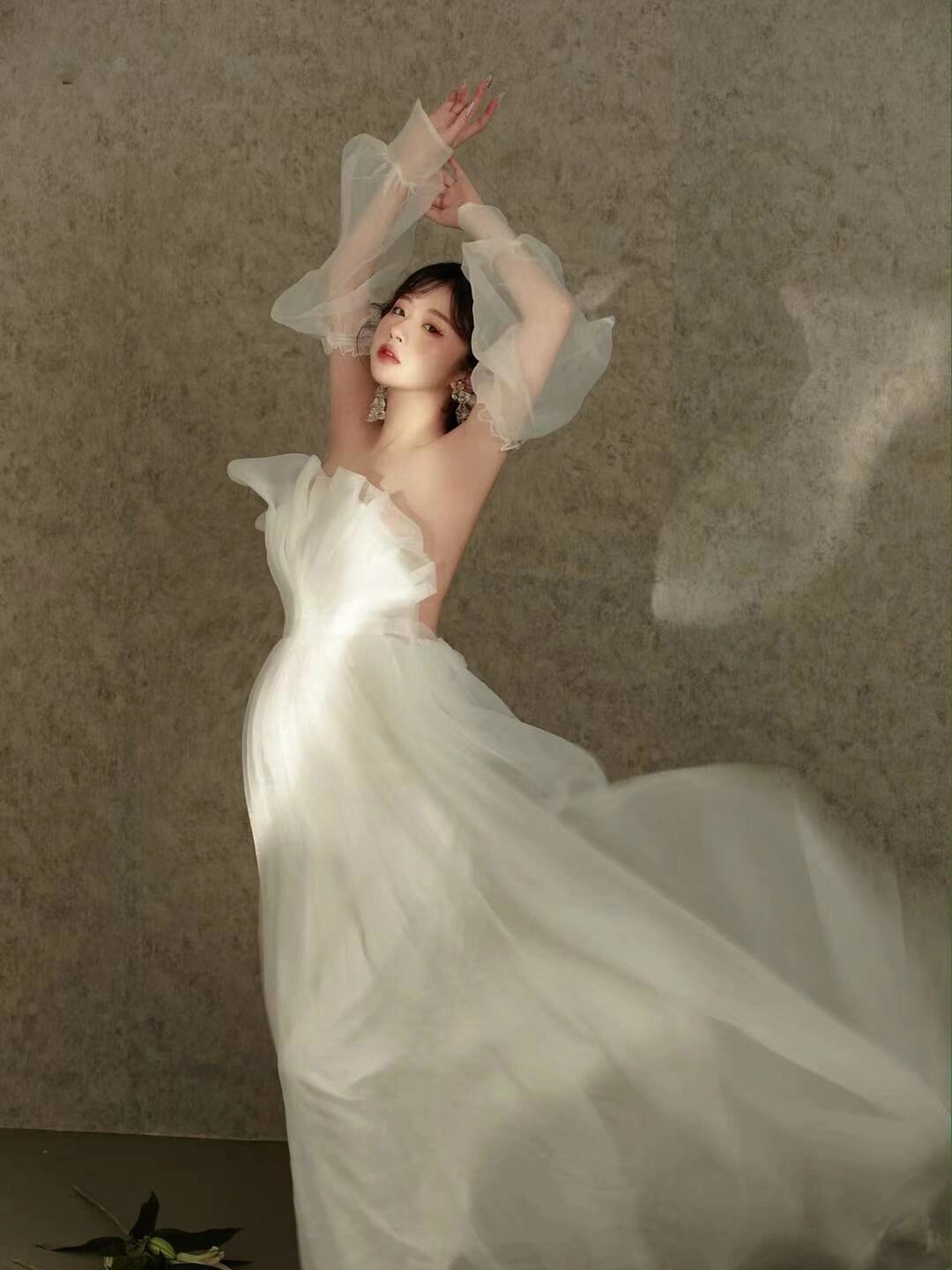 Woman in flowing white tulle gown with sheer sleeves raised gracefully in artistic bridal photo shoot.
