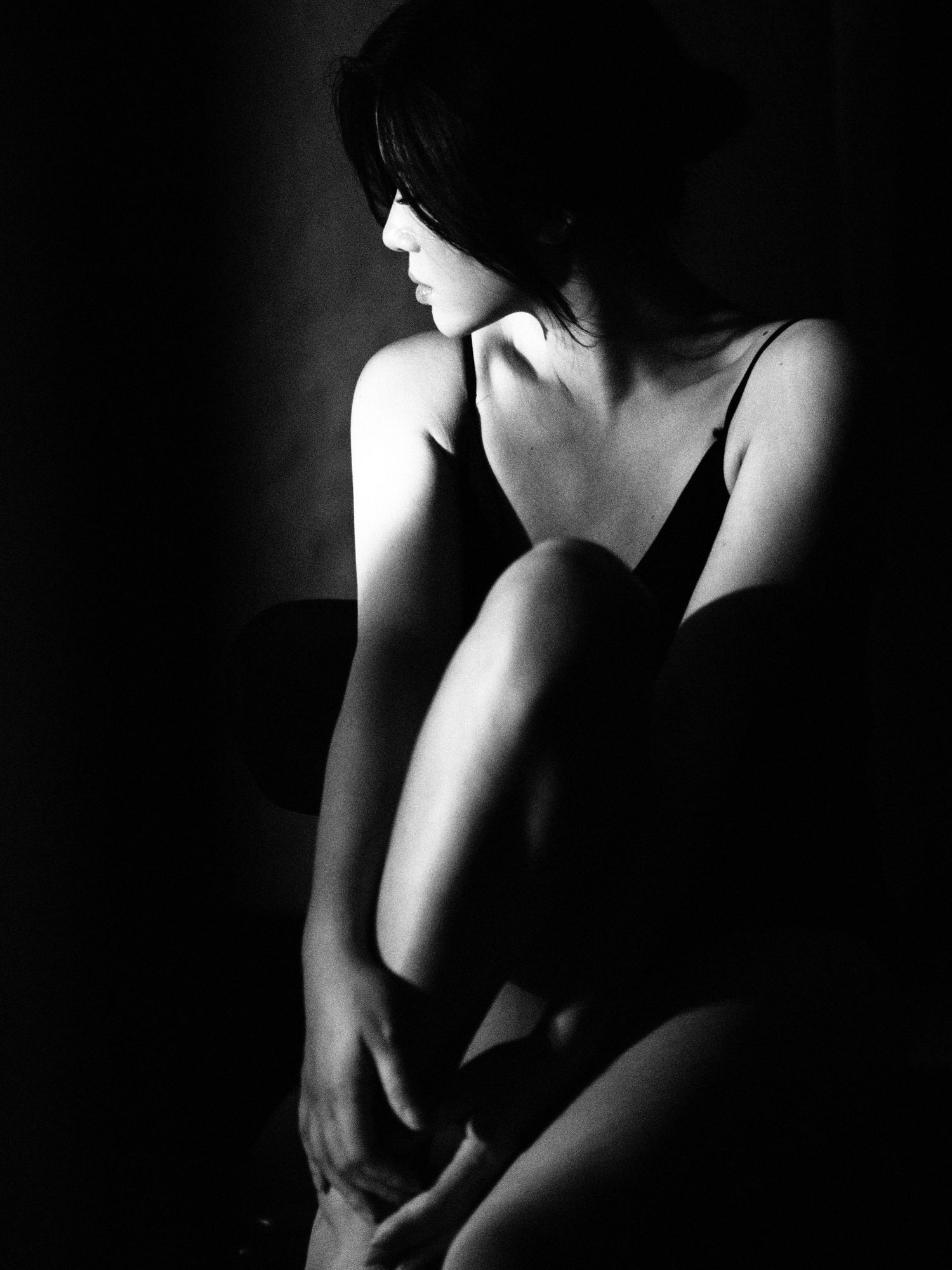 Artistic black and white silhouette of a woman sitting with knees drawn up in dramatic low-key lighting.