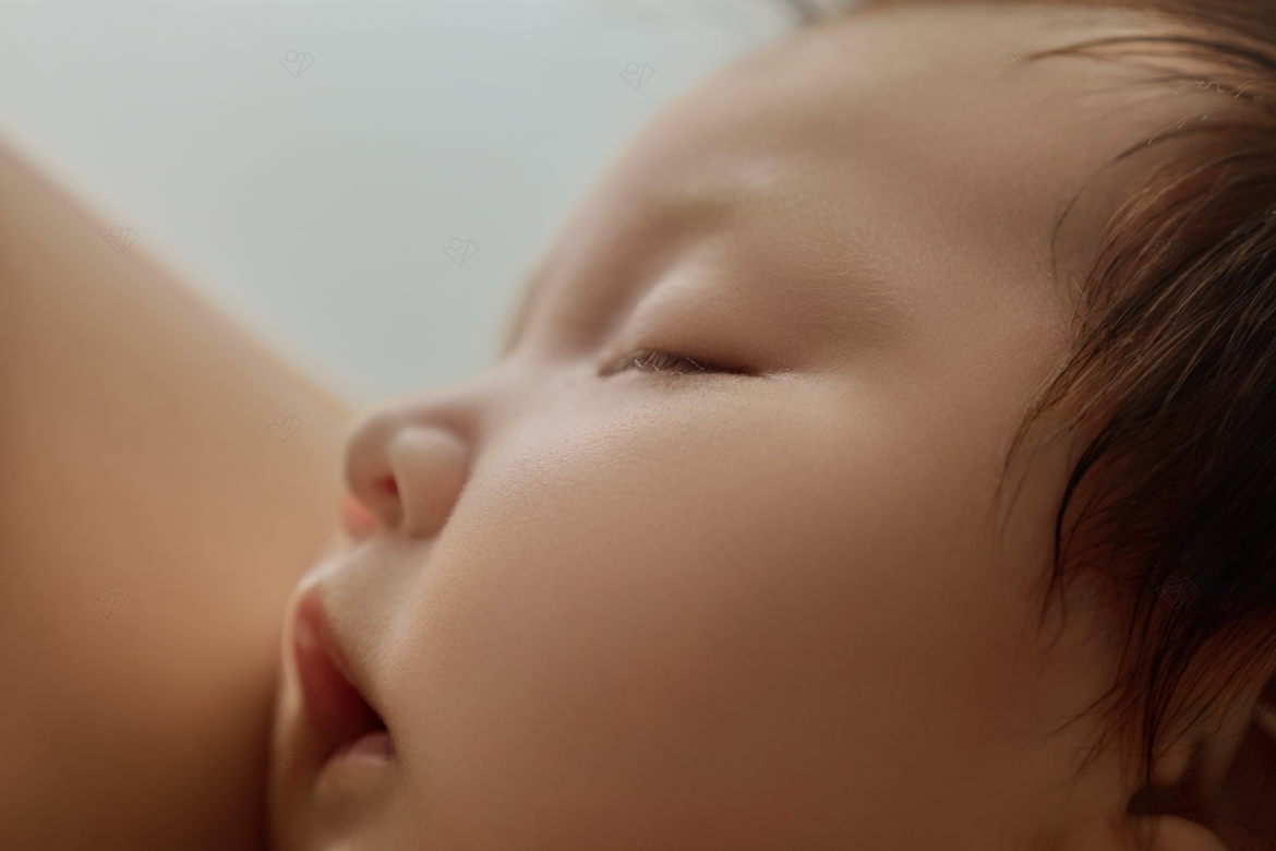Close-up of a peaceful sleeping newborn baby with soft skin and dark hair resting against a parent.