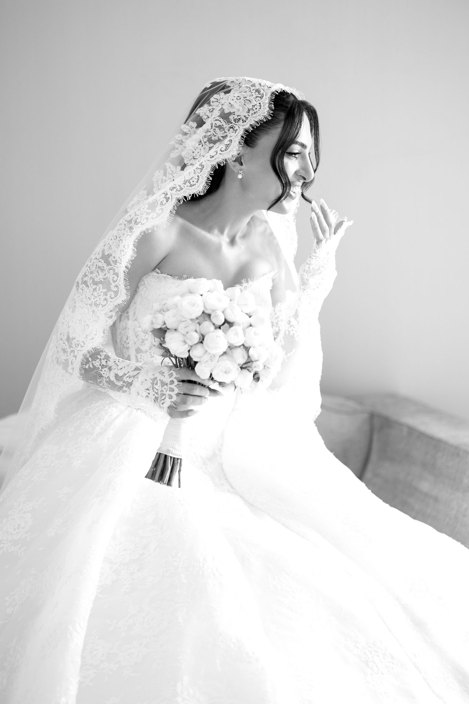 Black and white photo of a bride in a lace veil and gown holding a white bouquet.