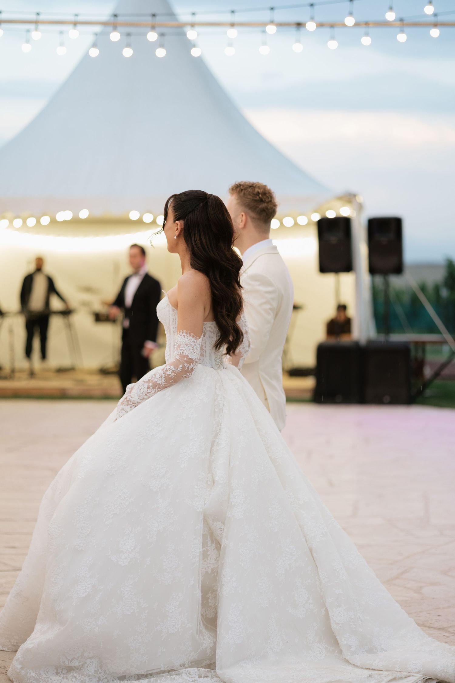 Bride in a stunning ballgown and groom in white tuxedo share their first dance at an outdoor evening wedding reception.