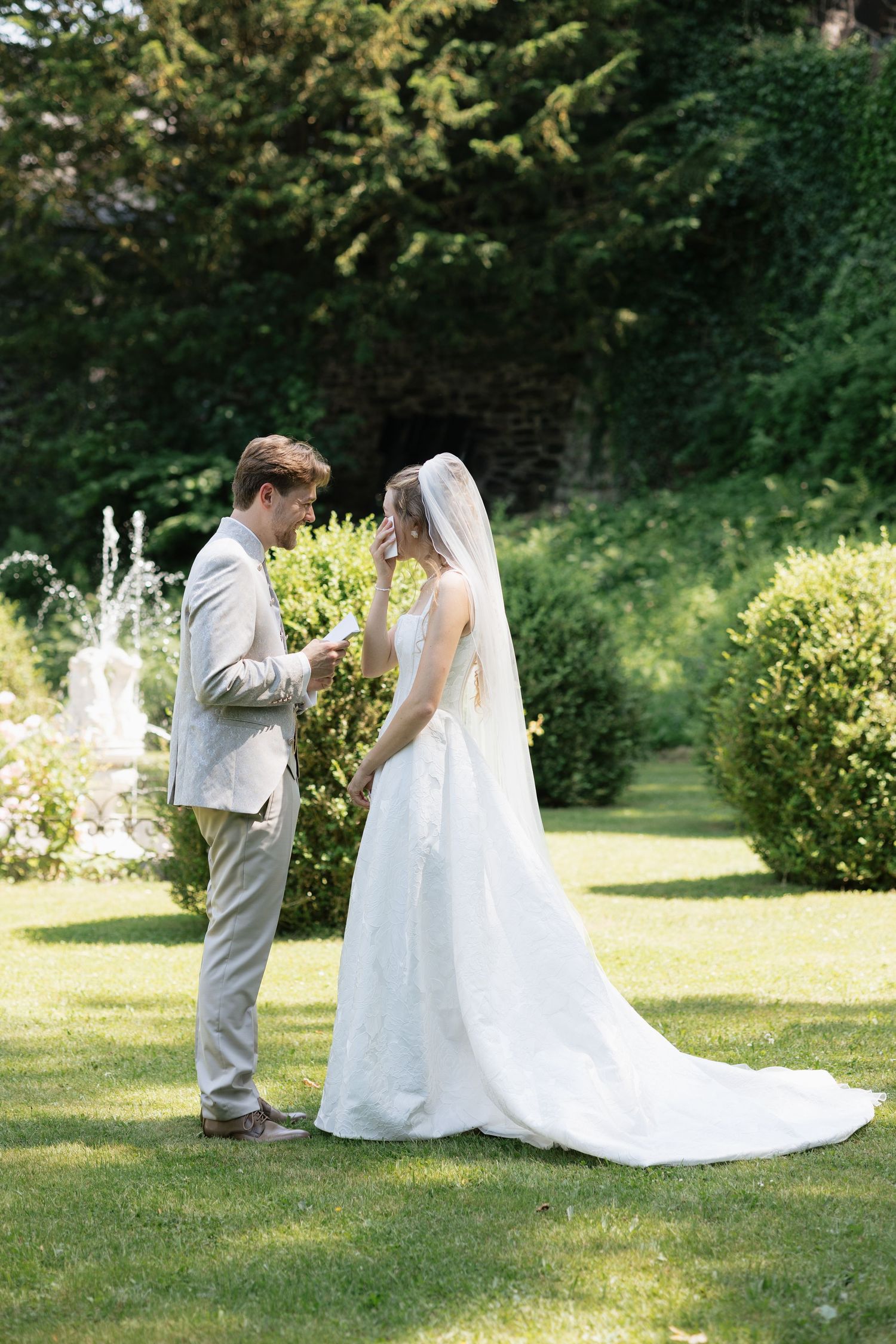 Bride and groom exchange vows in a lush garden setting, with the bride in a white gown and veil.