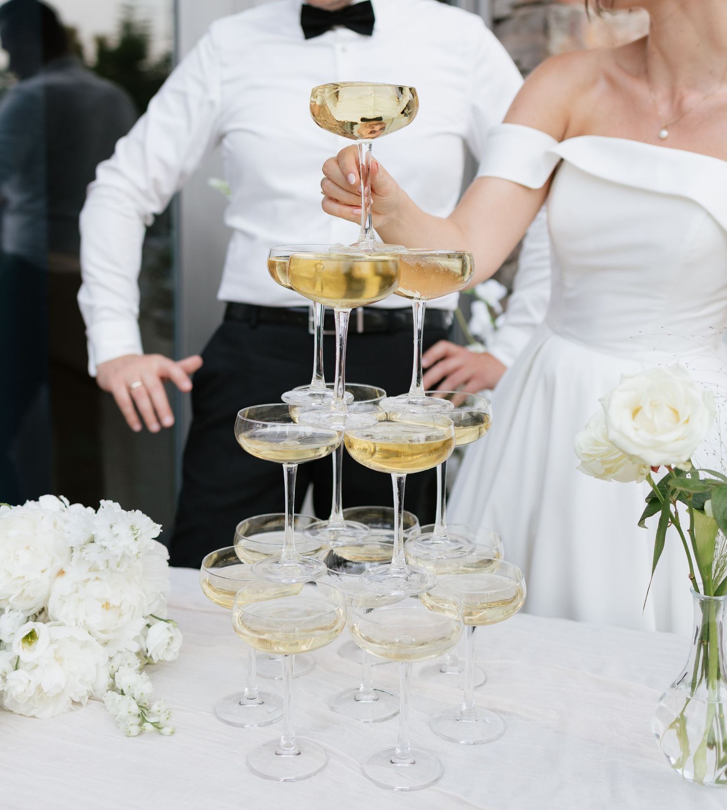 Bride and groom building a champagne tower with coupe glasses at a wedding reception.
