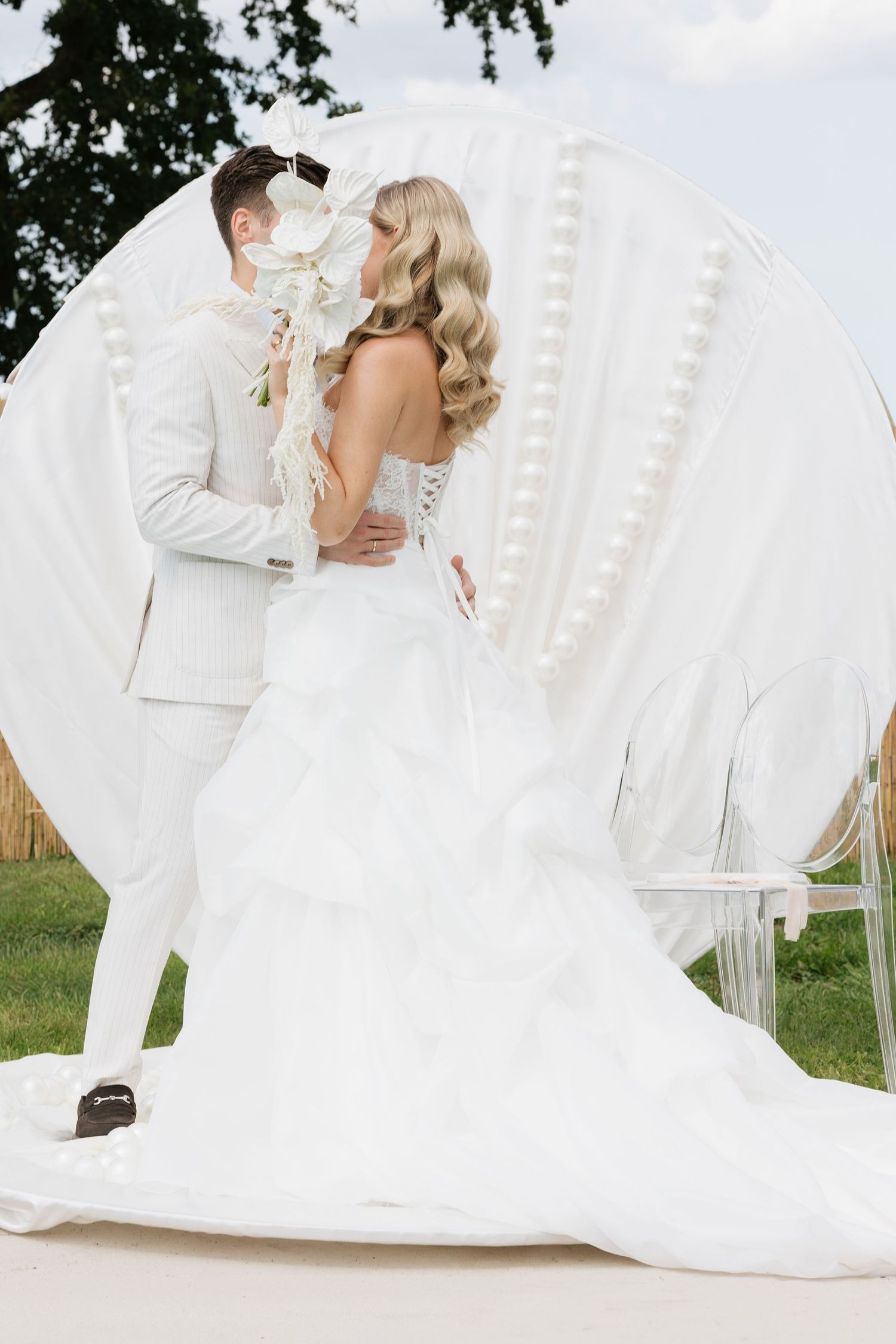 Bride and groom sharing a kiss in front of a white circular floral arch outdoors on their wedding day.