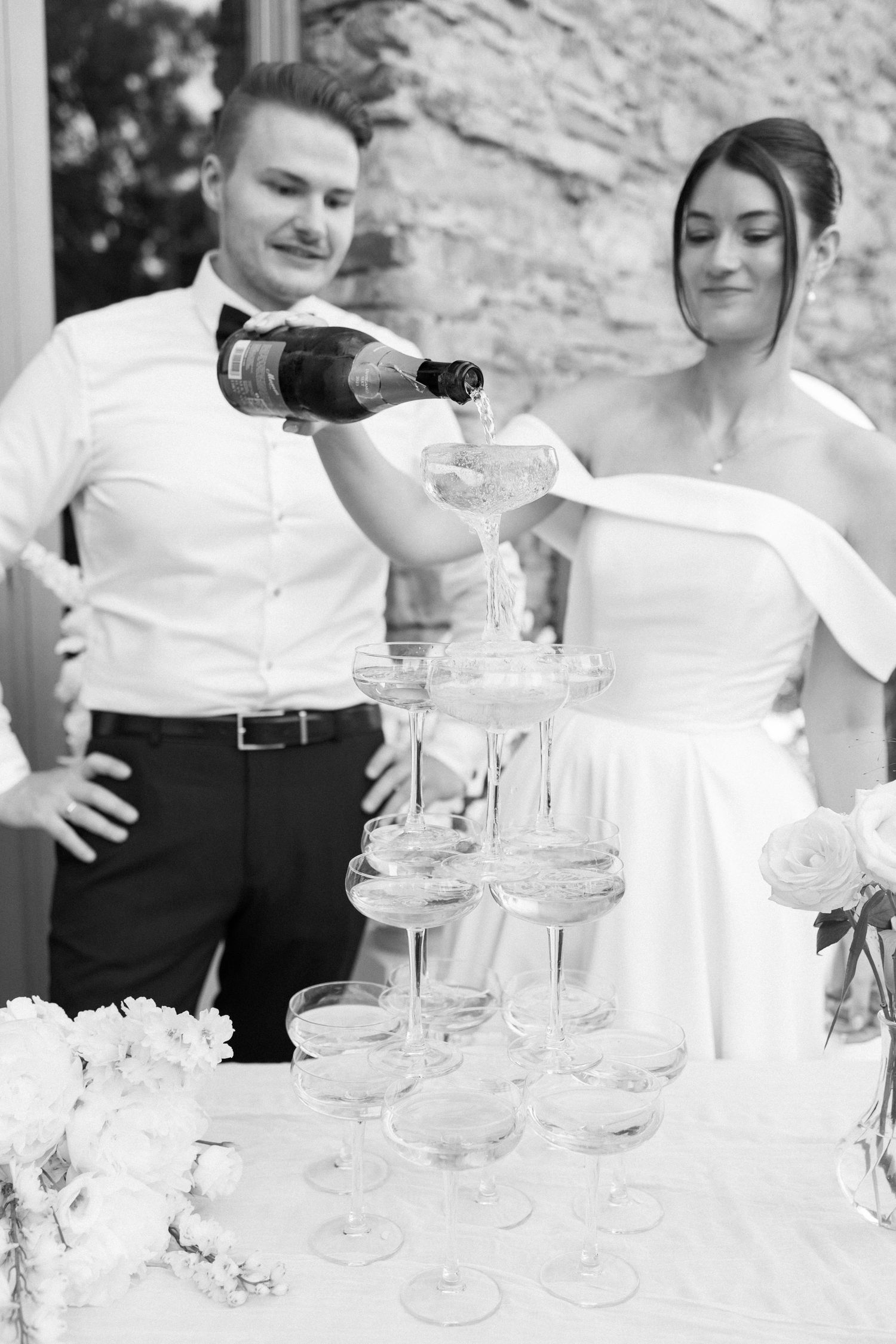 Bride and groom pouring champagne tower at wedding reception in black and white photo.