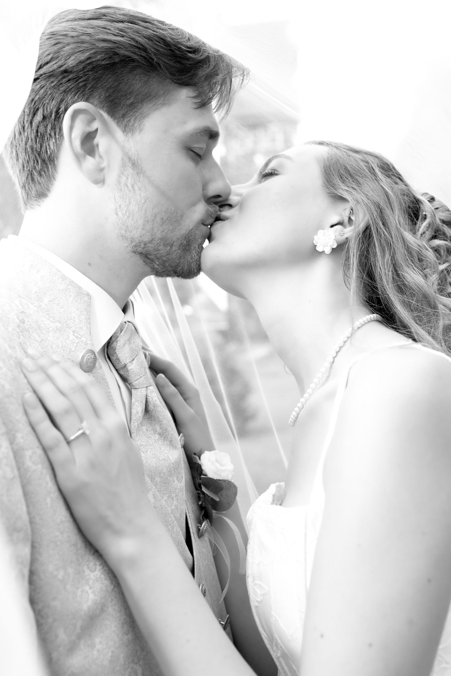 Black and white photo of a bride and groom sharing a romantic kiss on their wedding day.
