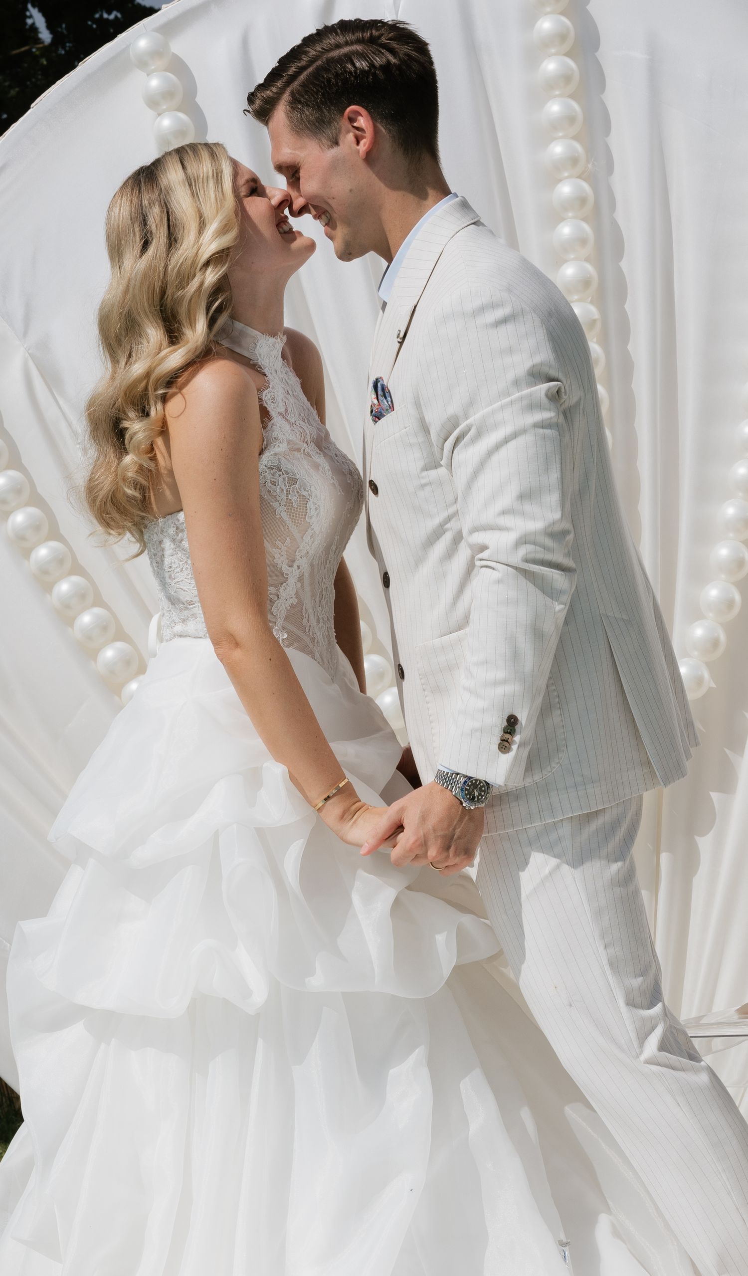 A bride and groom share a romantic moment at their elegant white wedding ceremony with pearl decorations.