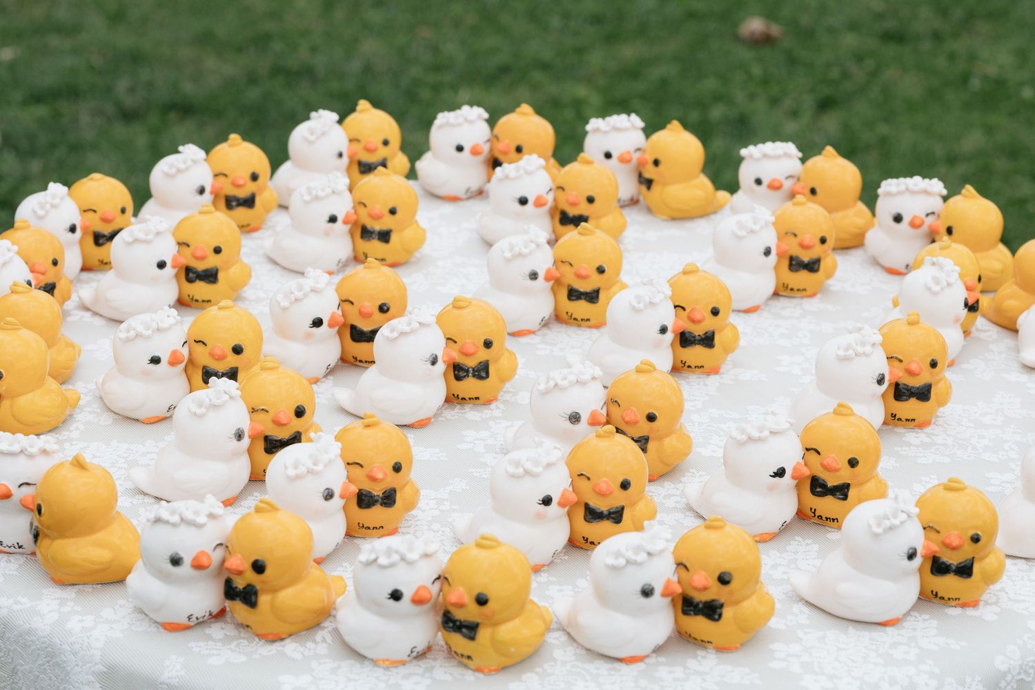 Miniature yellow rubber ducks dressed as bride and groom displayed on a white decorated wedding cake table.