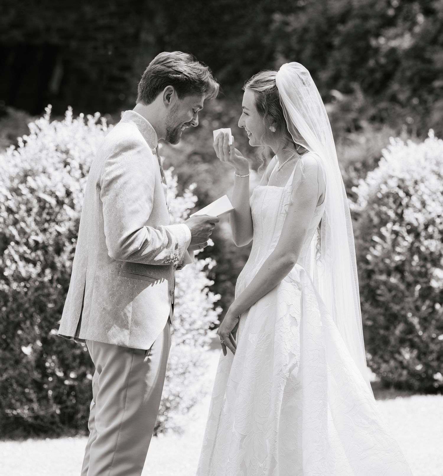 Black and white wedding photo of bride and groom sharing an emotional moment outdoors, bride in veil and white gown.