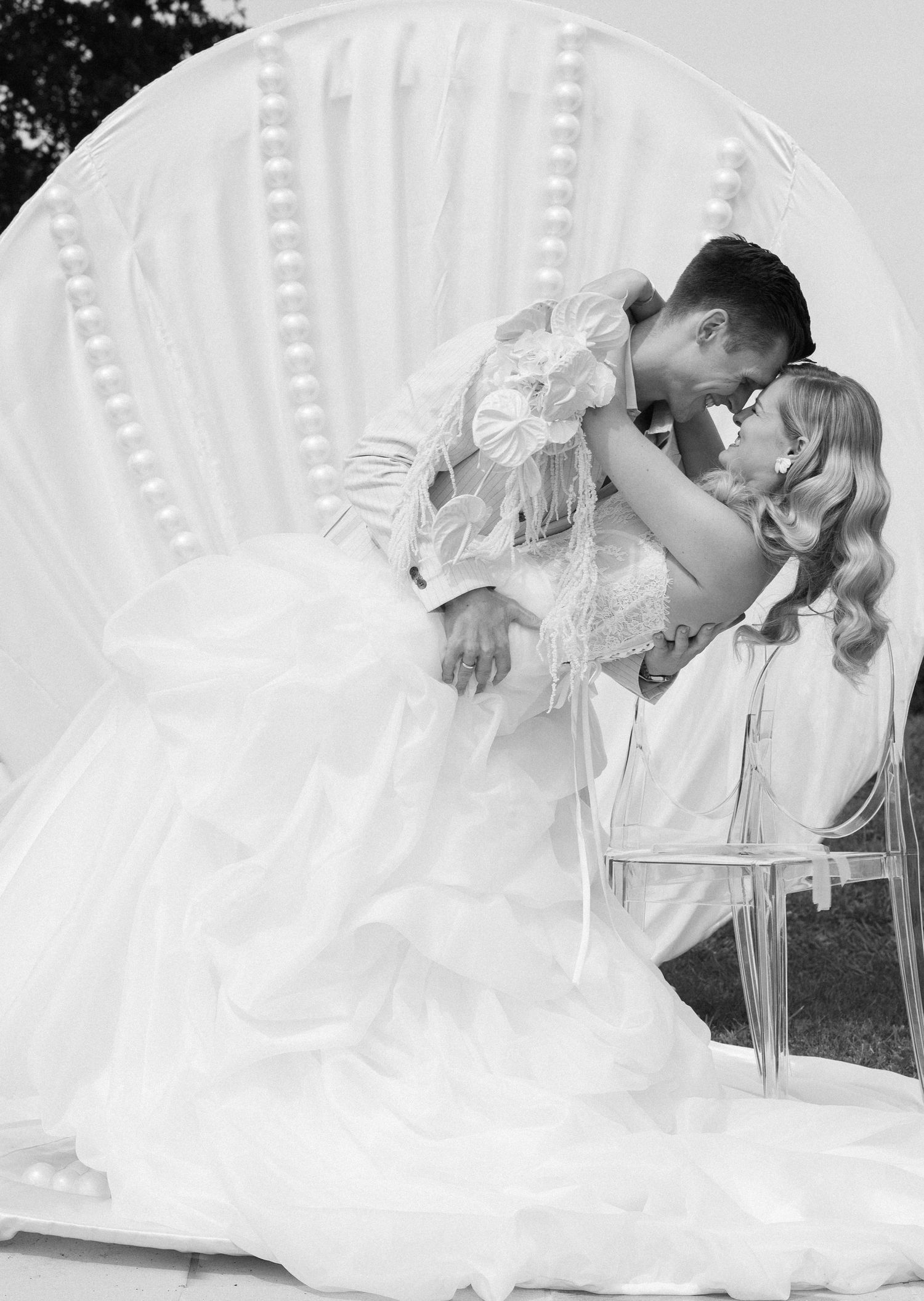 Black and white photo of a bride and groom sharing a romantic kiss in front of a decorative shell backdrop.