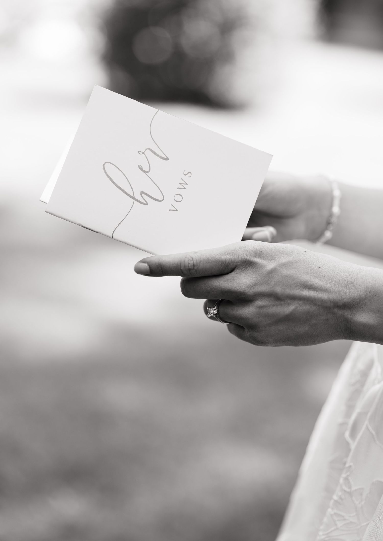 Bride holding her wedding vows booklet with engagement ring visible, black and white photo.