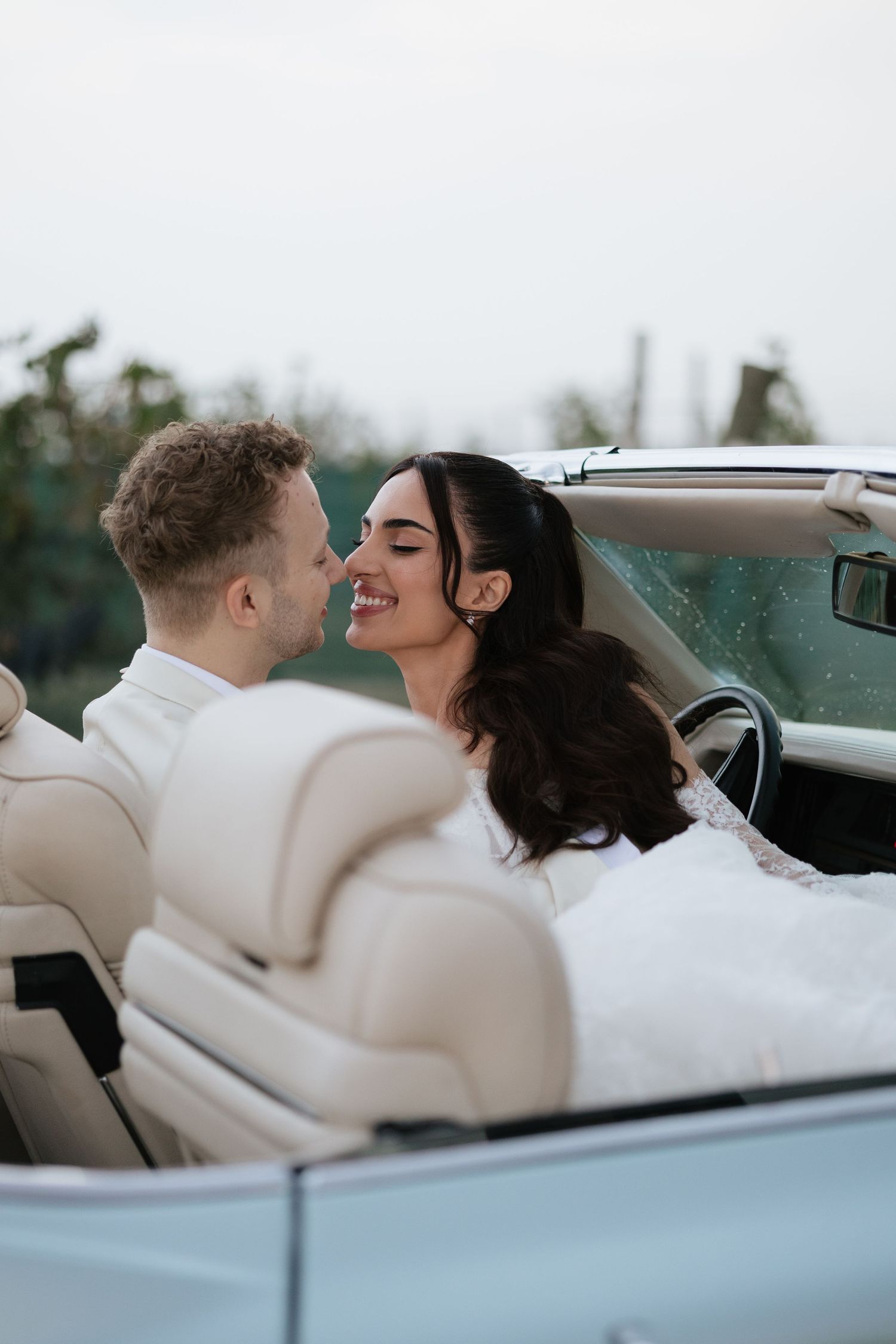 Bride and groom sharing a romantic moment in a white convertible car on their wedding day.