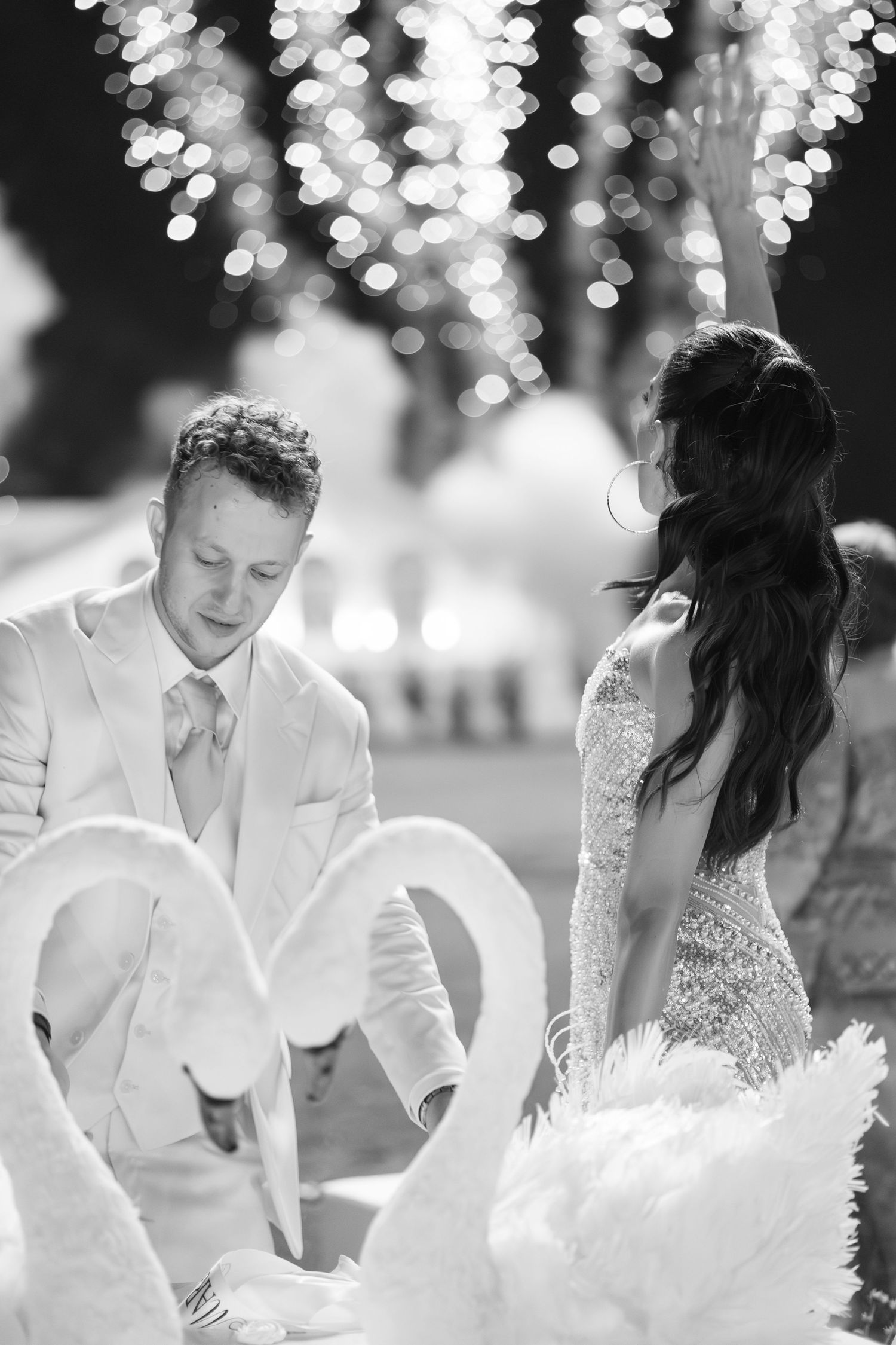 Black and white photo of a bride and groom with two white swans forming a heart shape at their wedding reception.