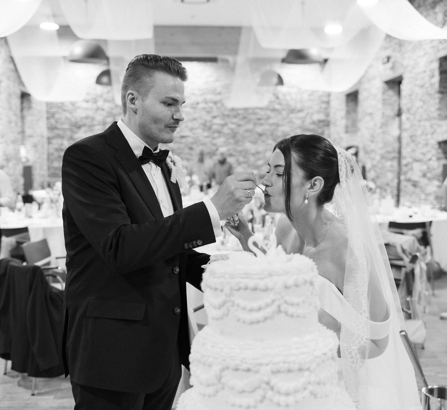 Bride and groom cutting white wedding cake together in elegant black and white wedding reception photo.