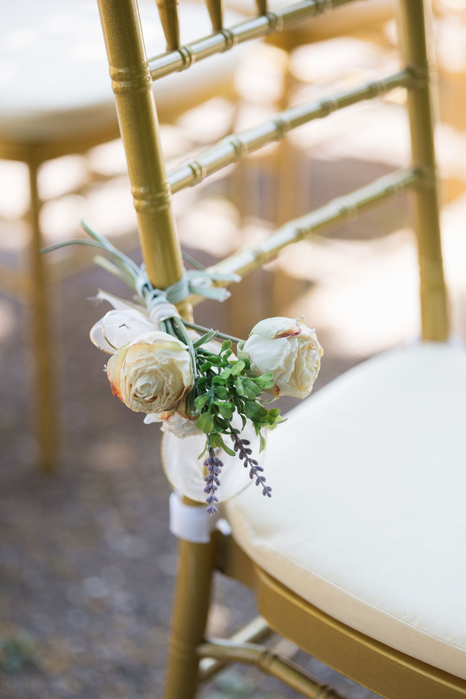 Gold chiavari chair decorated with white roses, greenery, and lavender for an elegant outdoor wedding ceremony.