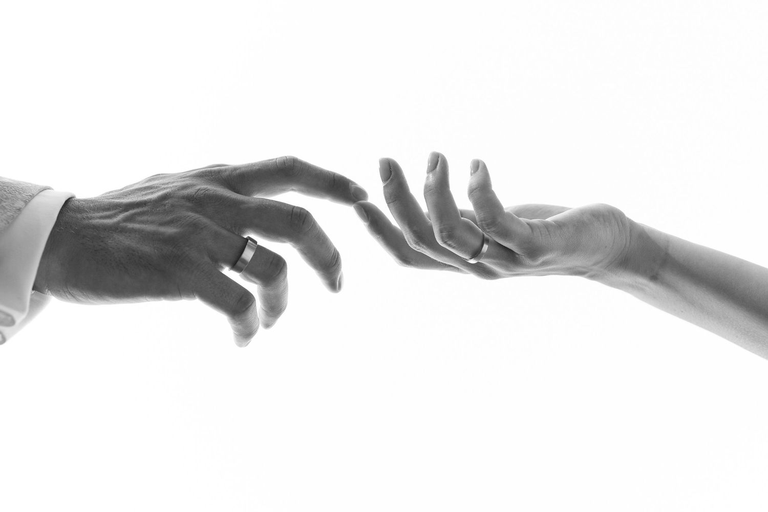 Black and white photo of two hands reaching toward each other, one wearing a wedding ring, symbolizing love and connection.