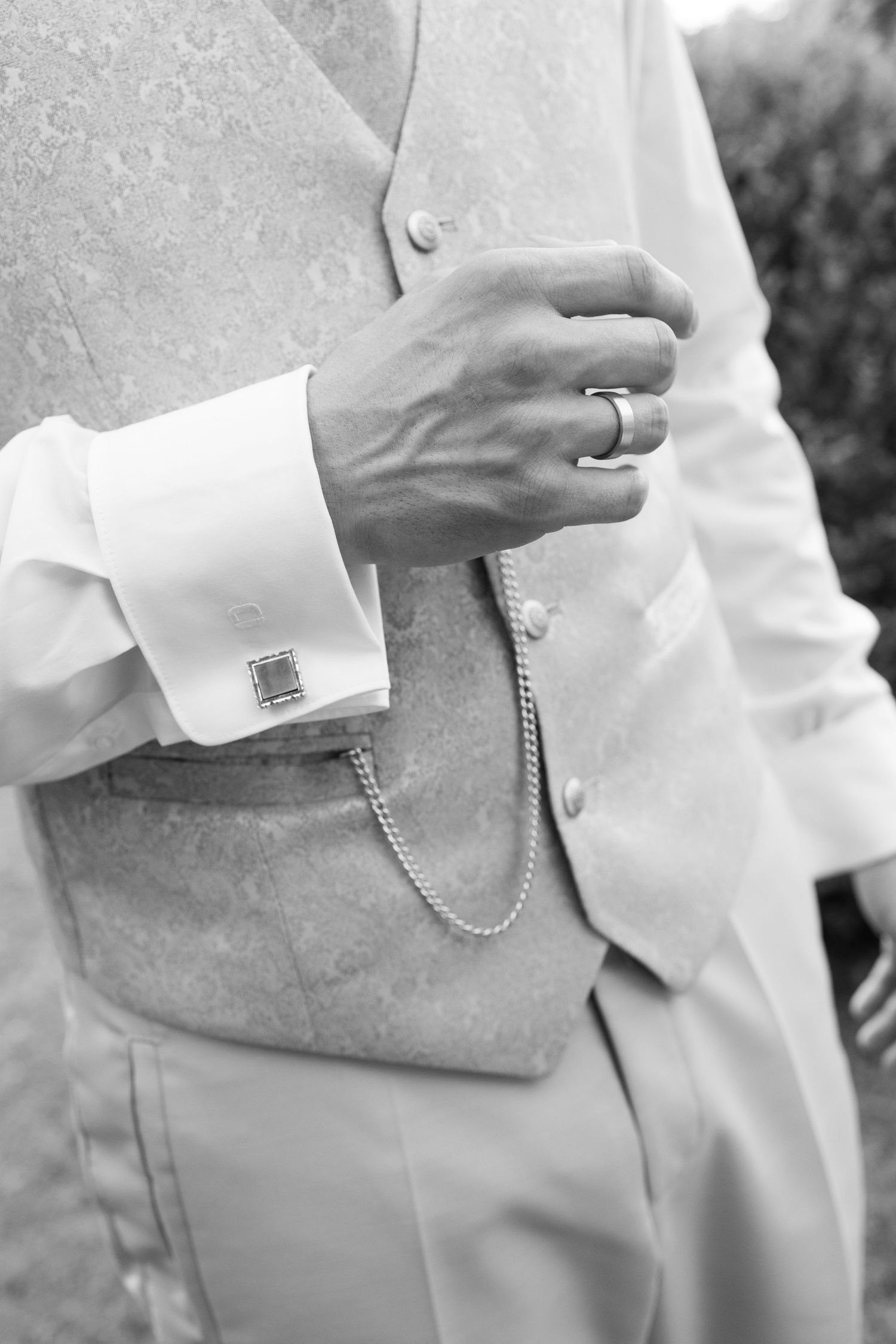 Black and white photo of groom in elegant vest with cufflinks, pocket watch chain, and wedding ring.