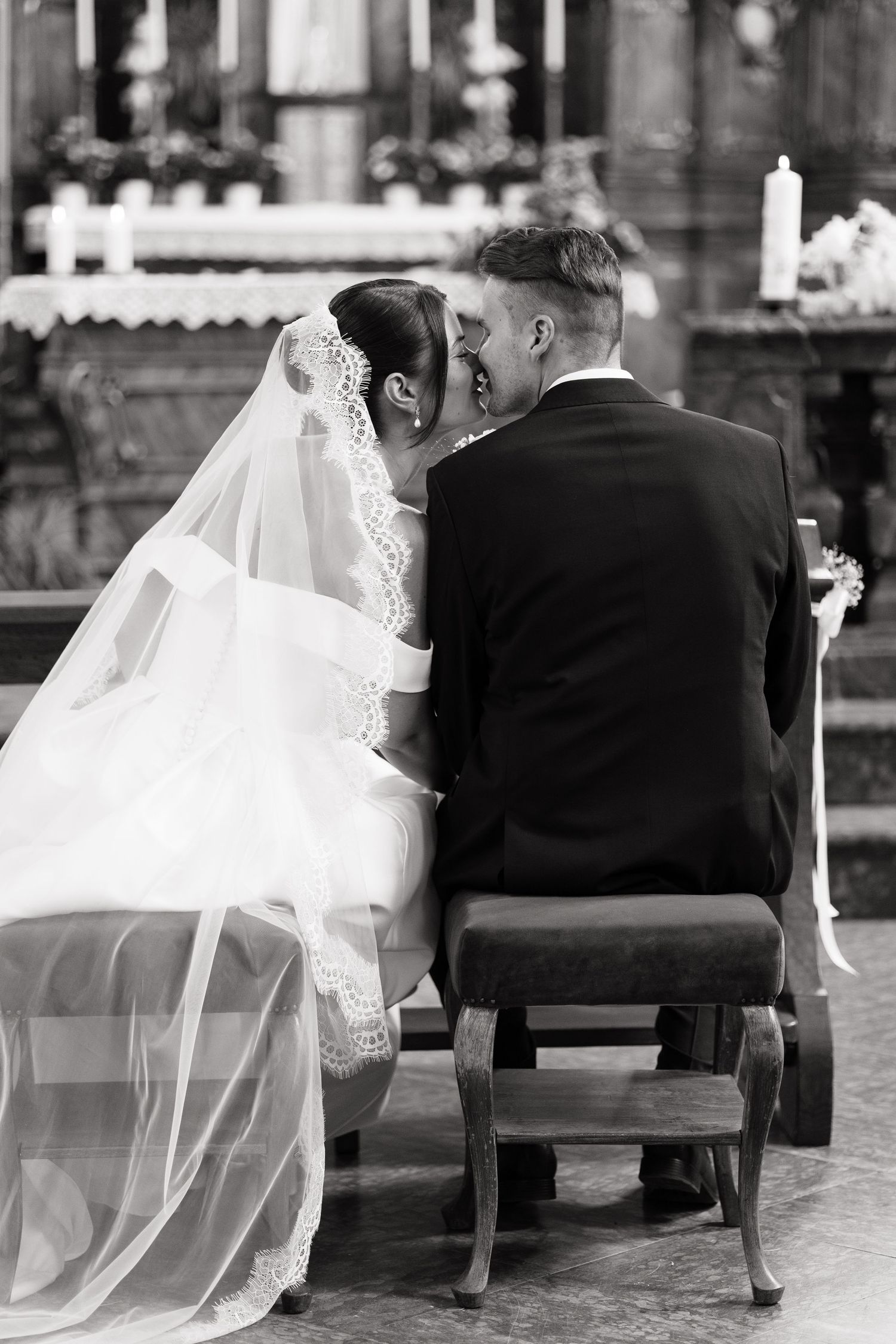 Black and white photo of bride and groom sitting together at church altar during wedding ceremony.