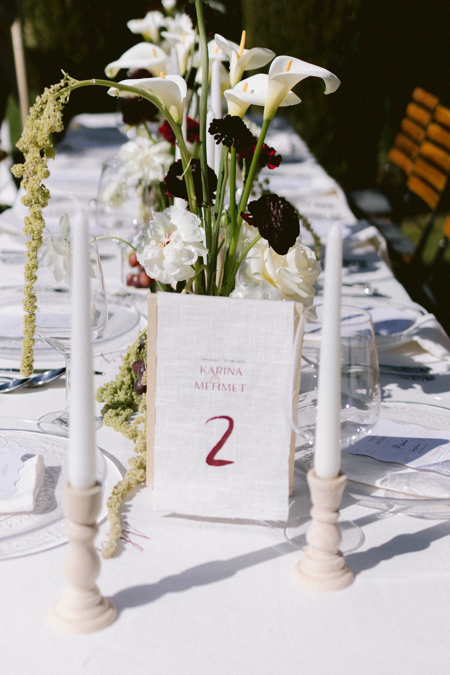 Elegant wedding table setting with white calla lilies, candles, and a table number card reading Karina and Mehmet, Table 2.