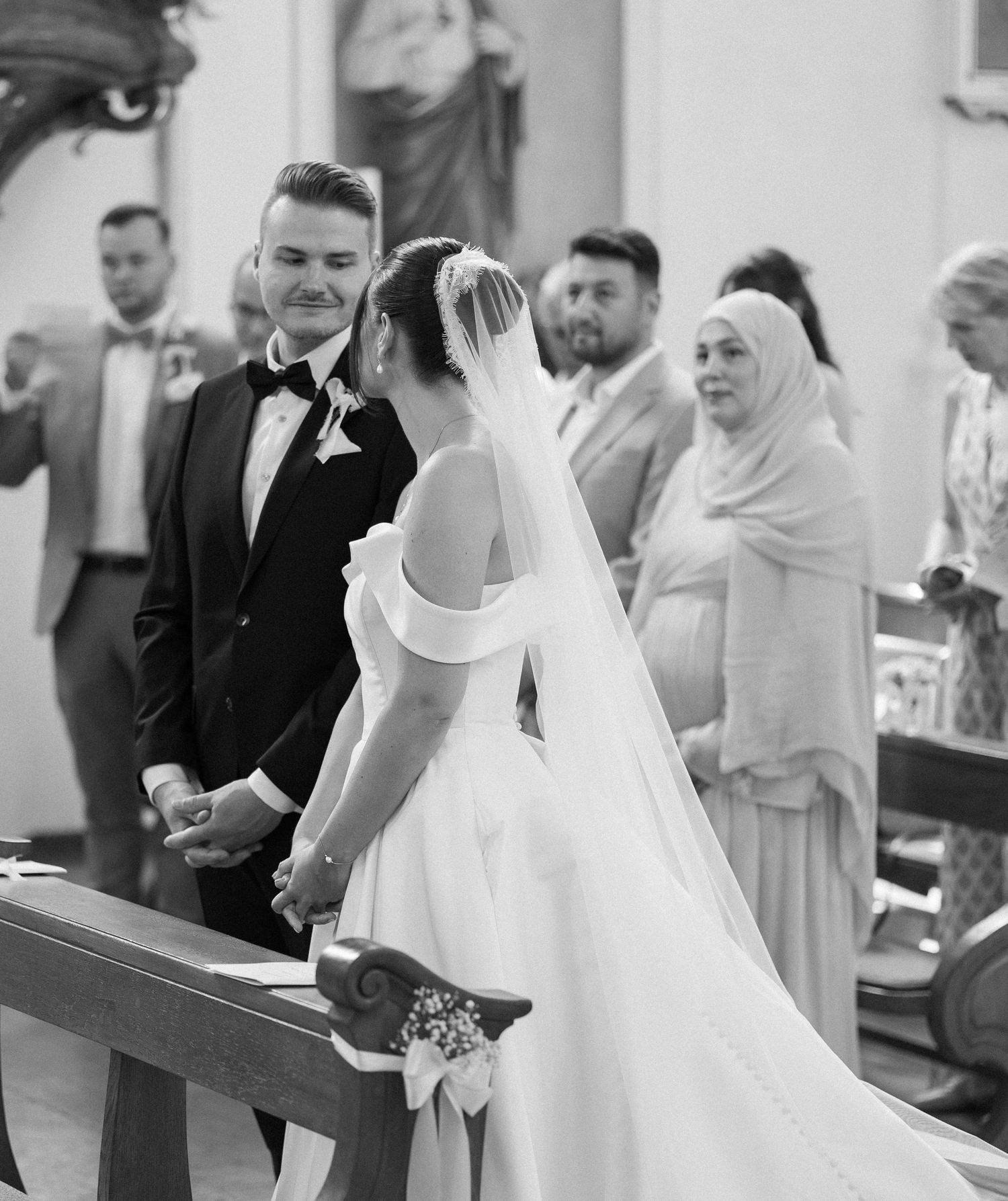 Black and white wedding ceremony photo of bride and groom holding hands at the altar in a church.