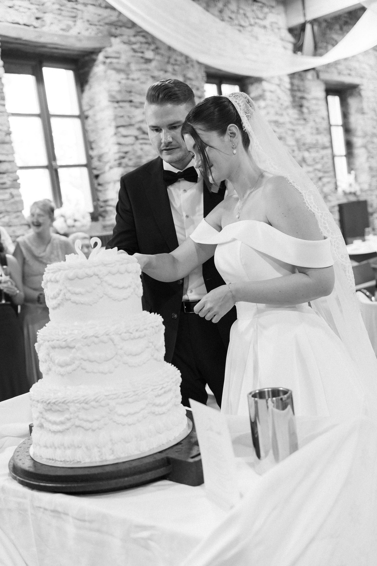 Black and white photo of bride and groom cutting their elegant three-tiered white wedding cake at their reception.