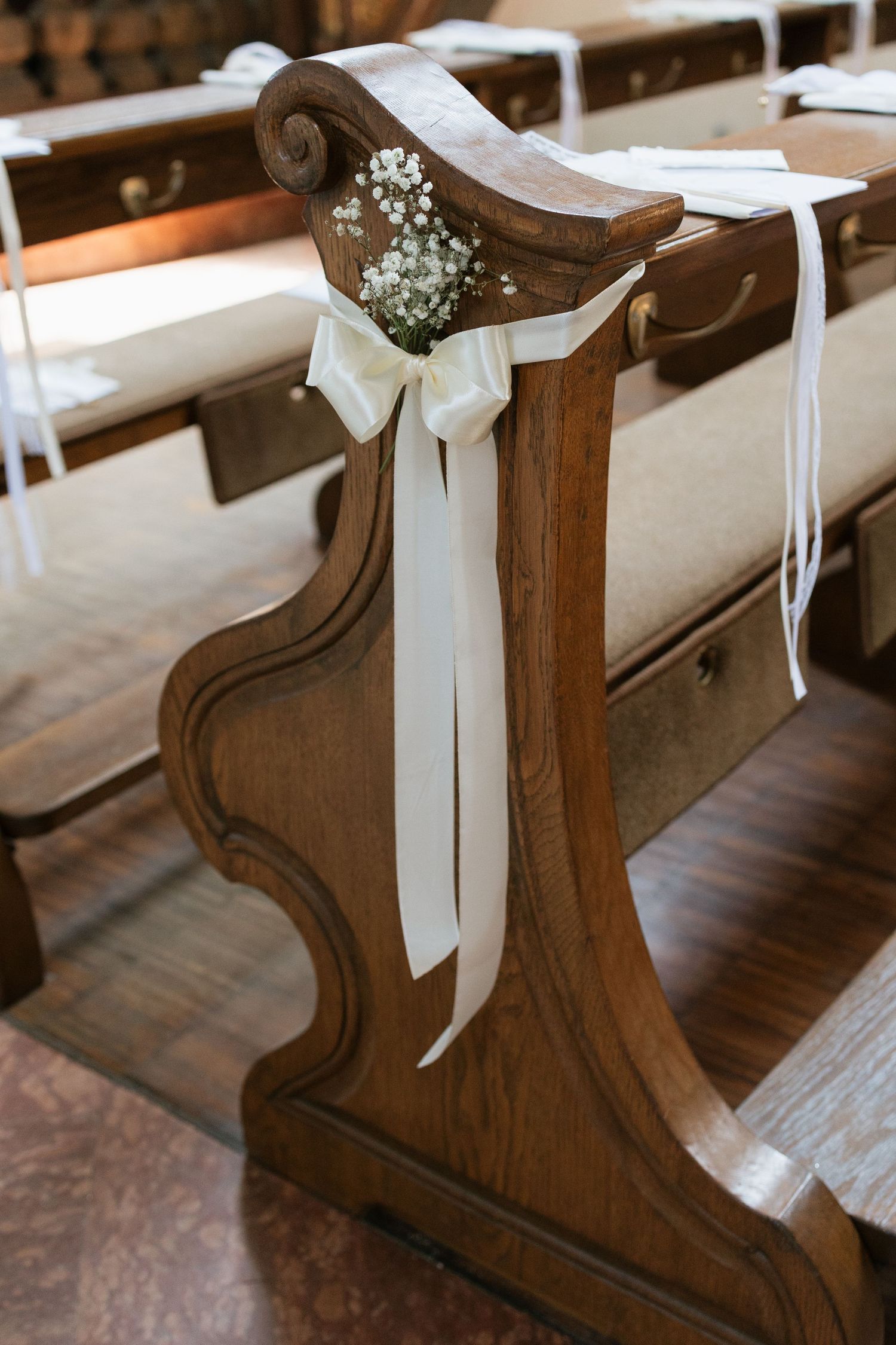 Elegant wooden church pew decorated with white ribbon bow and baby's breath flowers for a wedding ceremony.