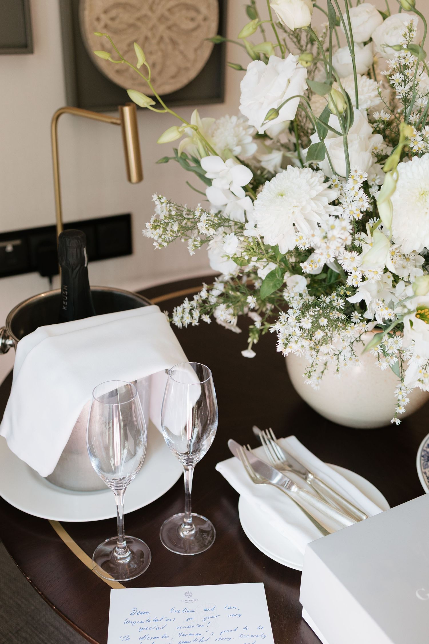 Elegant table setting with white floral centerpiece, crystal glasses, silverware, and neatly folded napkins on a dark table.