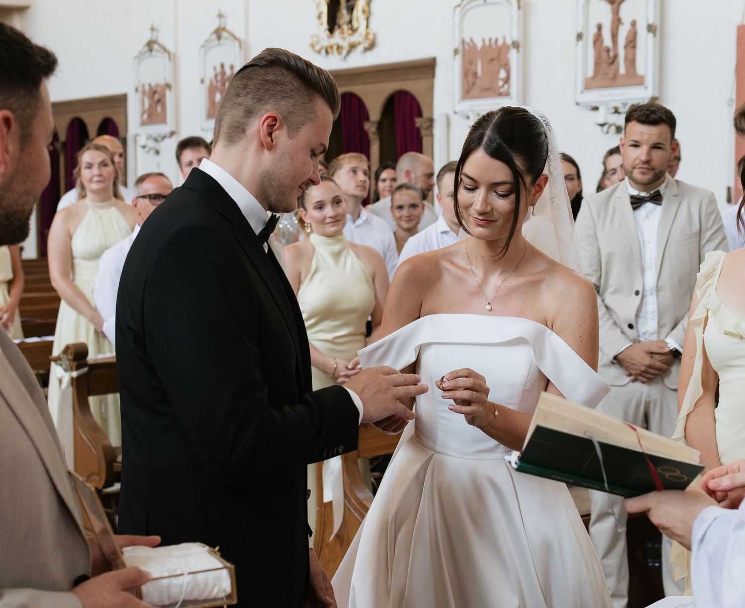 Bride and groom exchanging rings during a church wedding ceremony, surrounded by guests in elegant attire.