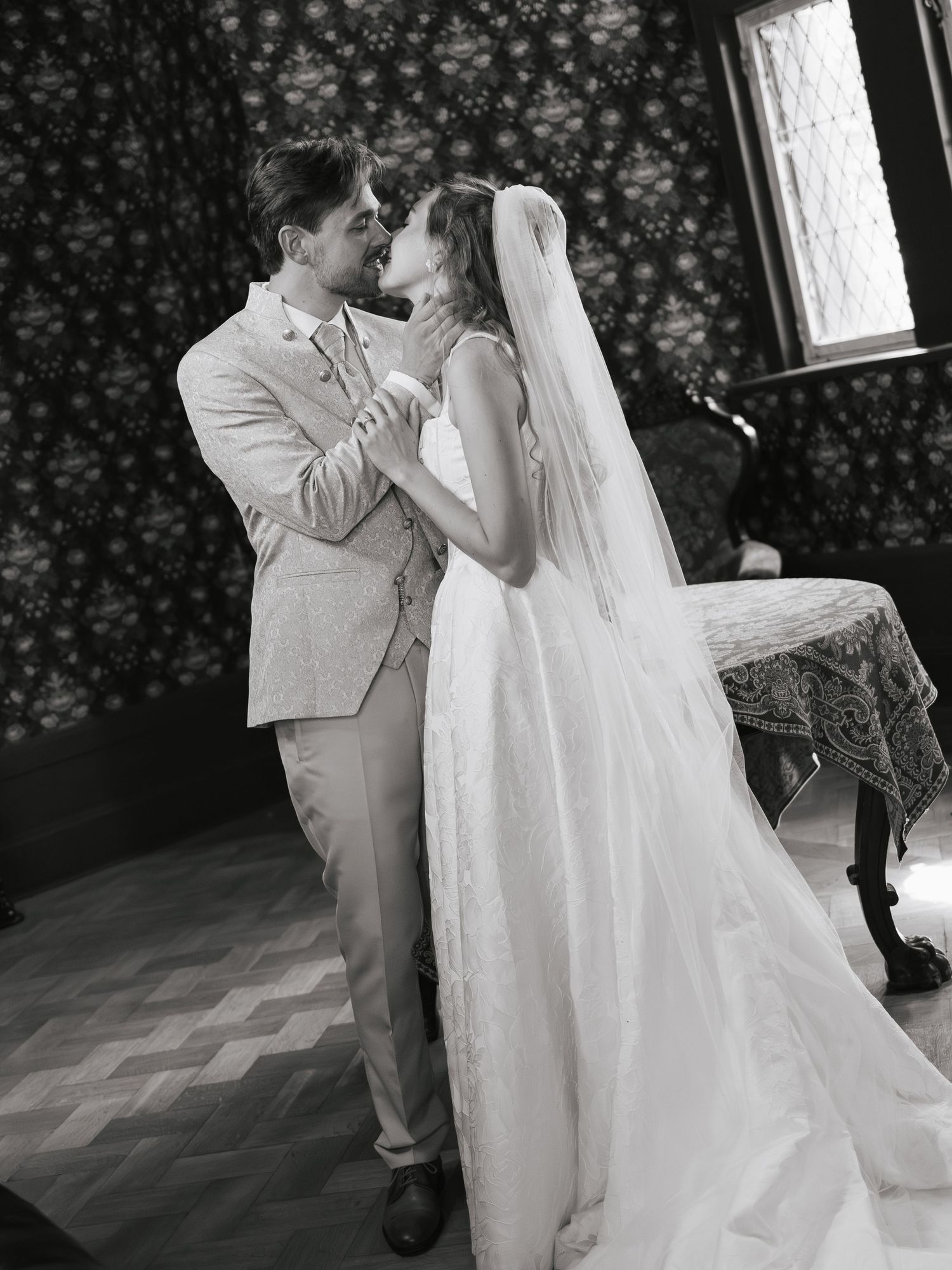 Black and white photo of a bride and groom sharing a tender kiss during their first dance at an elegant wedding venue.