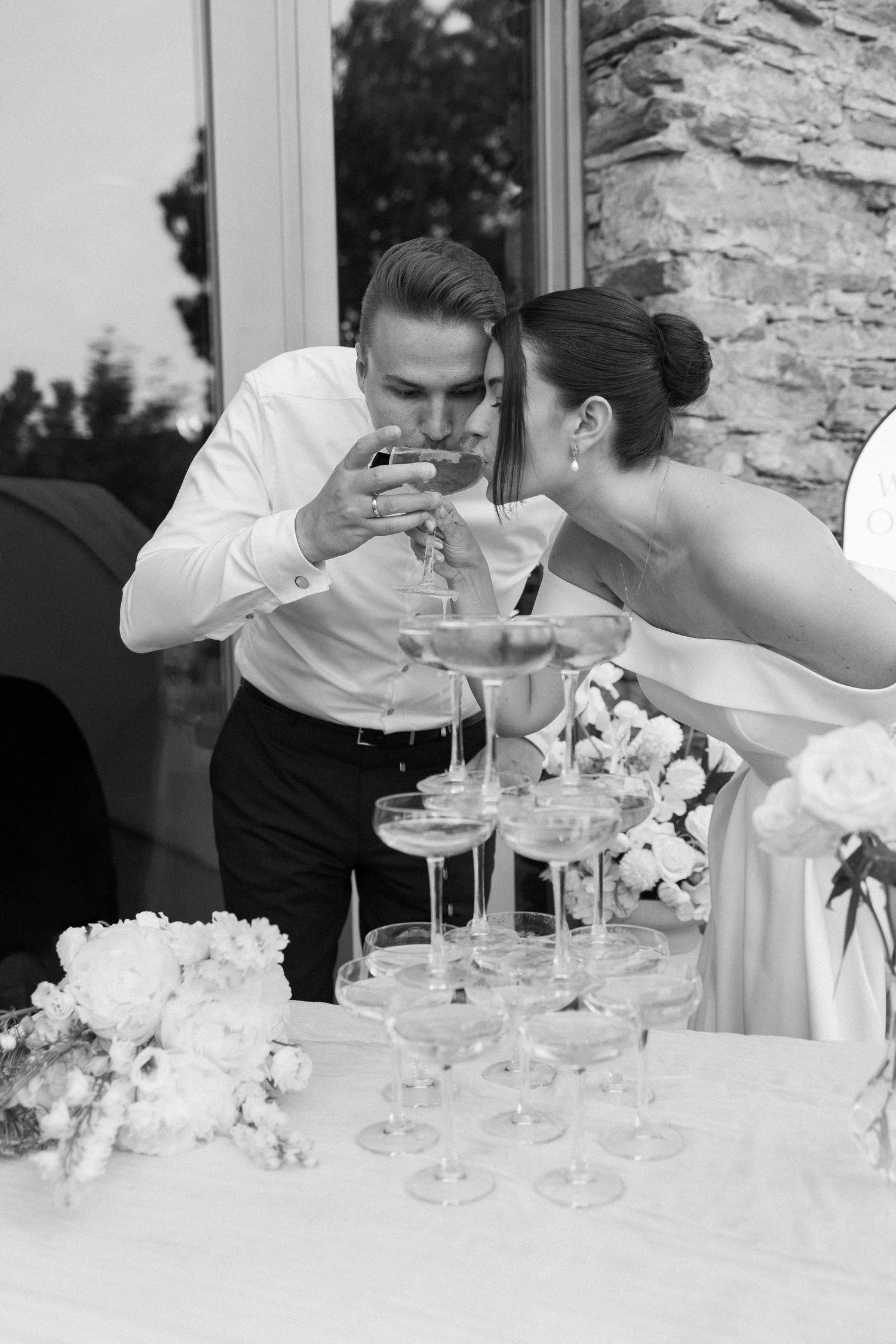 Black and white photo of bride and groom pouring champagne tower at wedding reception.