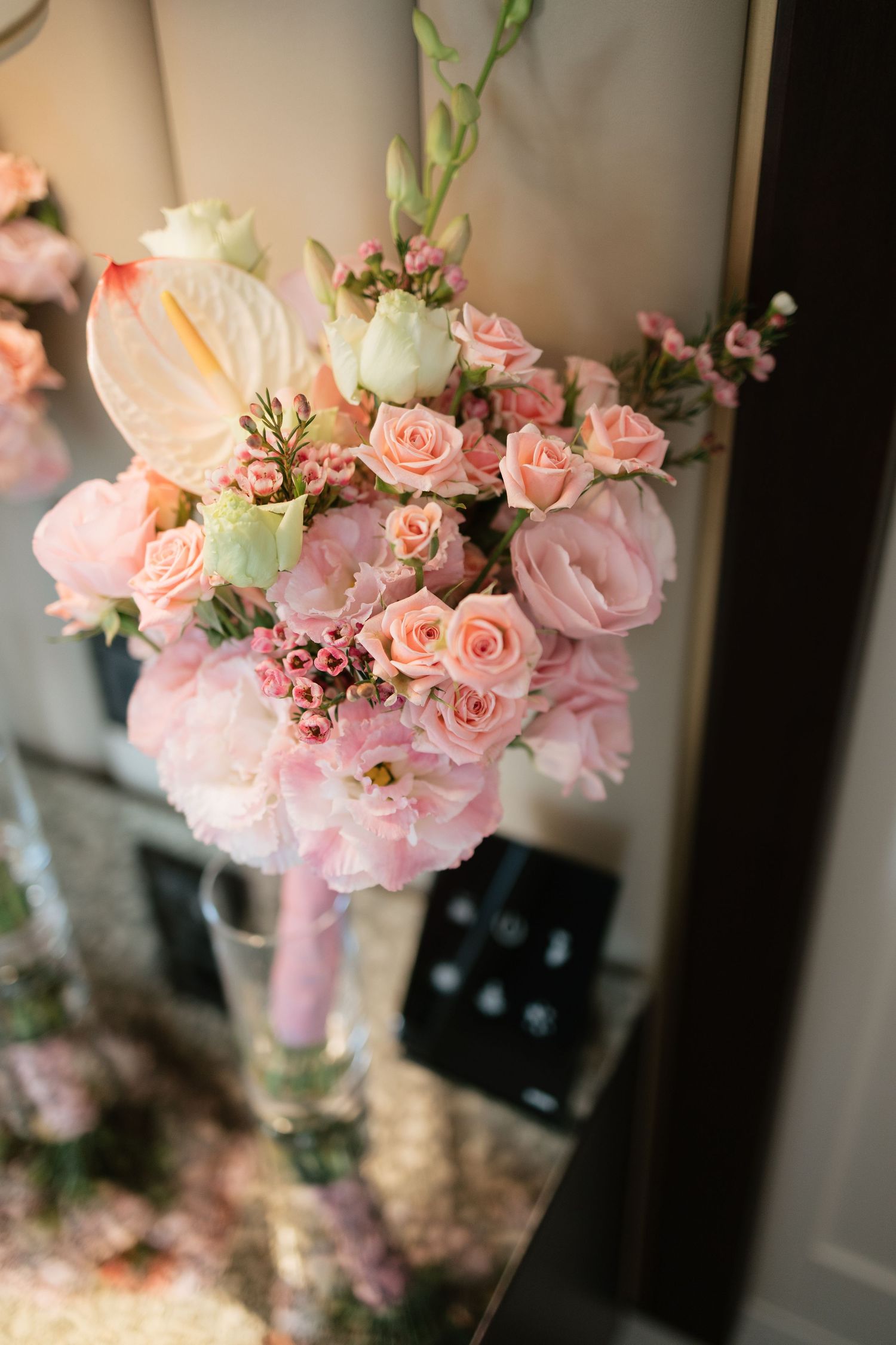 Elegant pink floral arrangement with roses, peonies, and anthurium in a glass vase for a wedding.