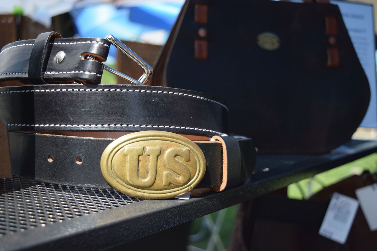 Closeup view of a black leather belt with brass buckle and white contrast stitching detail.