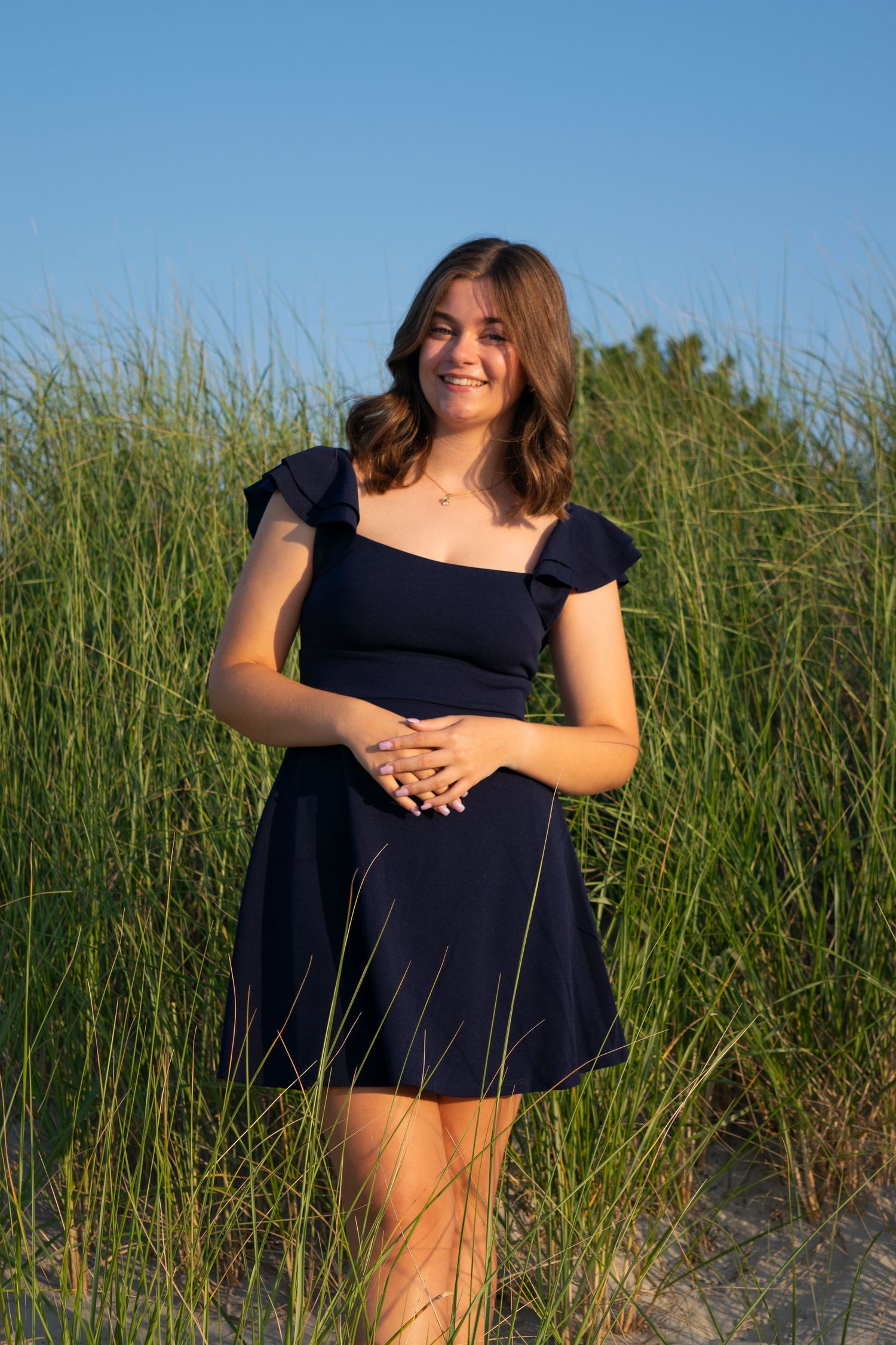 A person in a navy blue dress stands among tall beach grass on a sunny summer day.