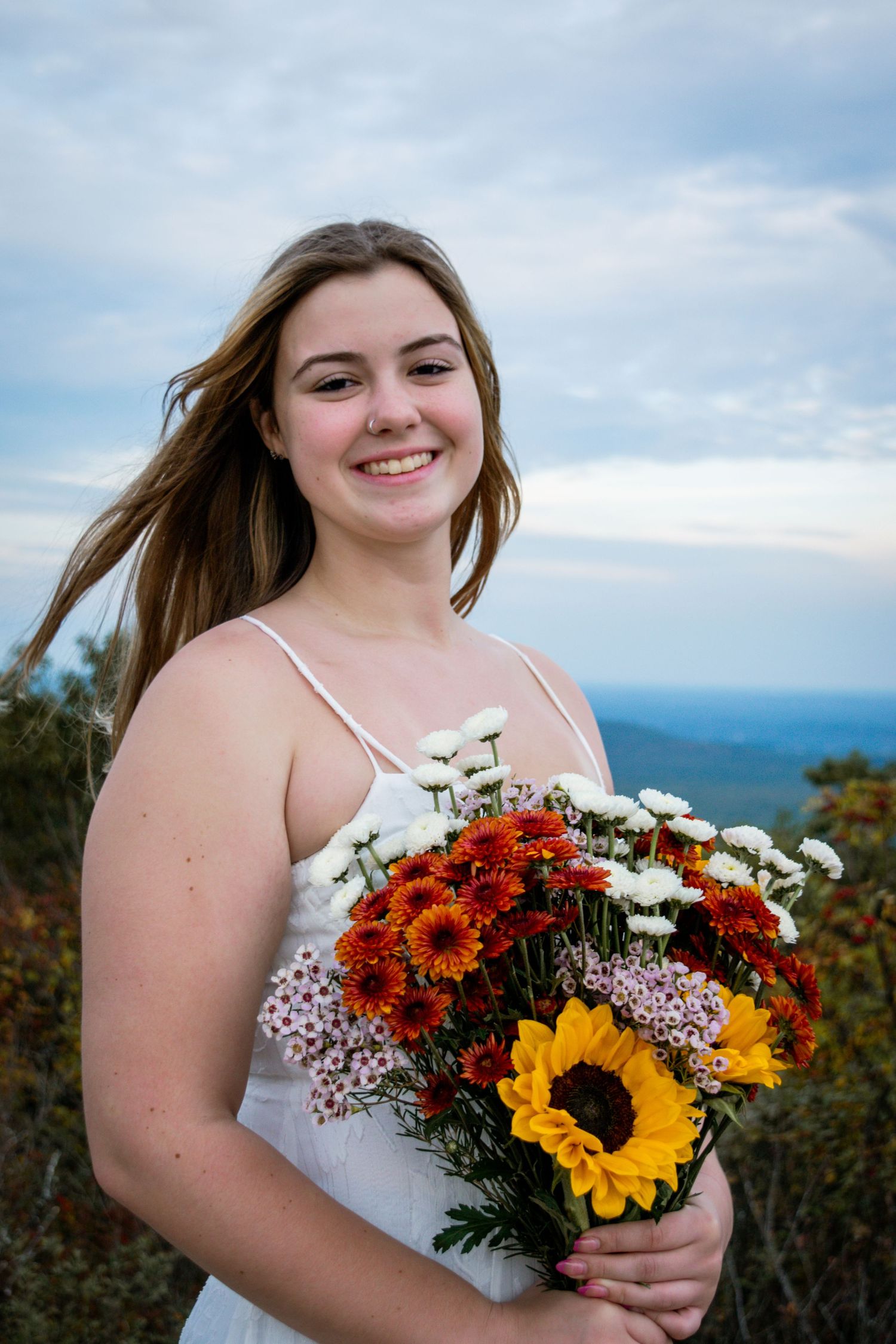 A vibrant autumn bridal bouquet featuring sunflowers, red daisies and white flowers against a mountain landscape backdrop.