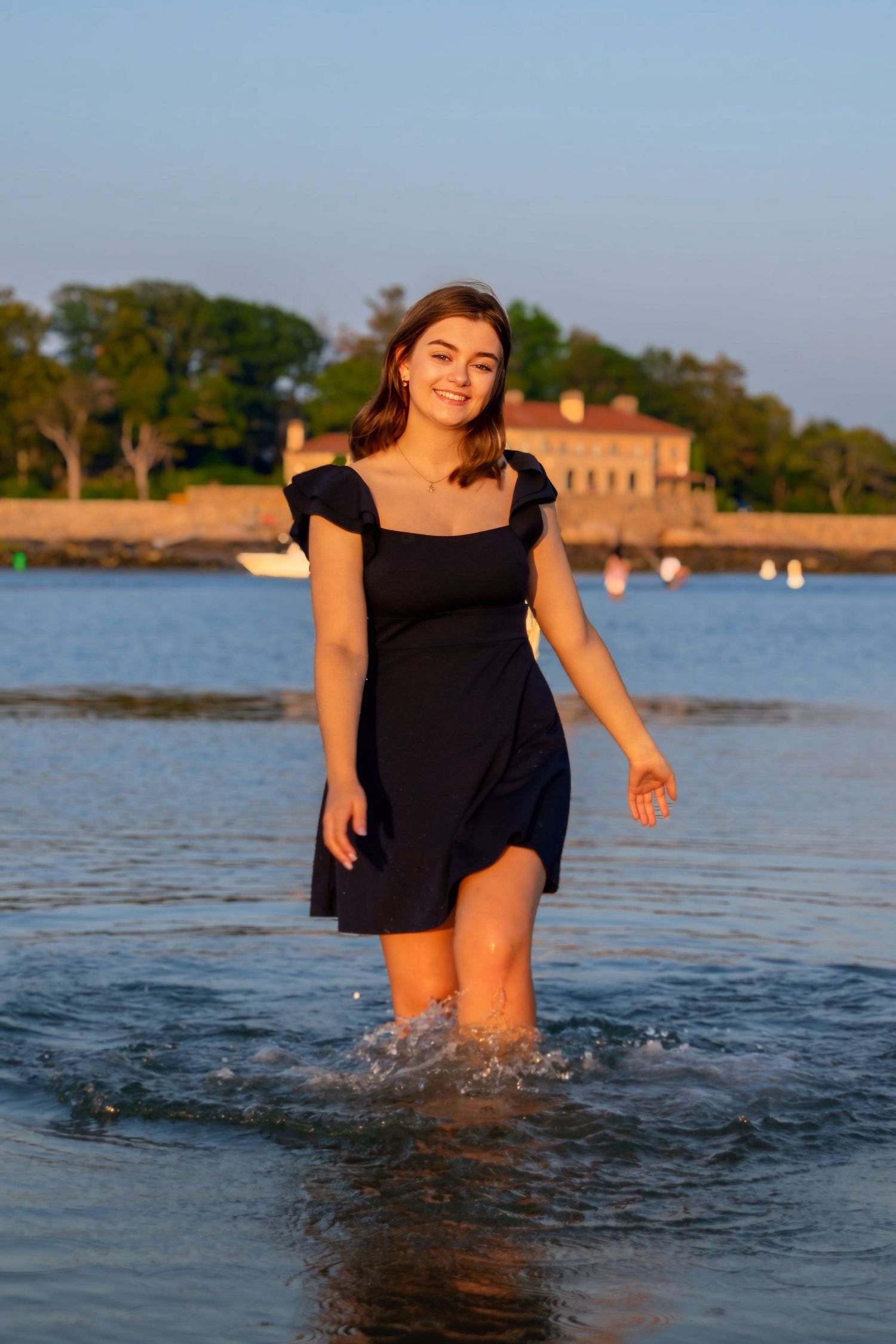 A person in a black dress splashes and plays in shallow lake water during sunset.