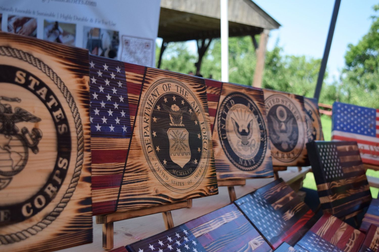 Wooden military service branch emblems displayed with American flags at an outdoor event.