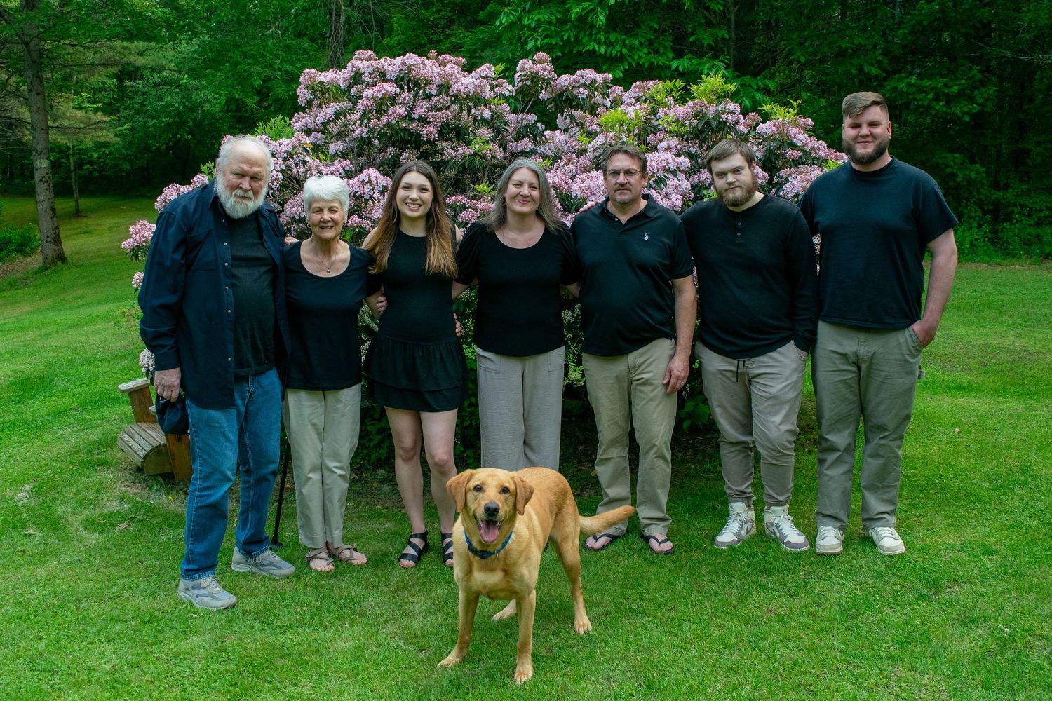 A group of people and a brown dog stand together on a green lawn for a photo.