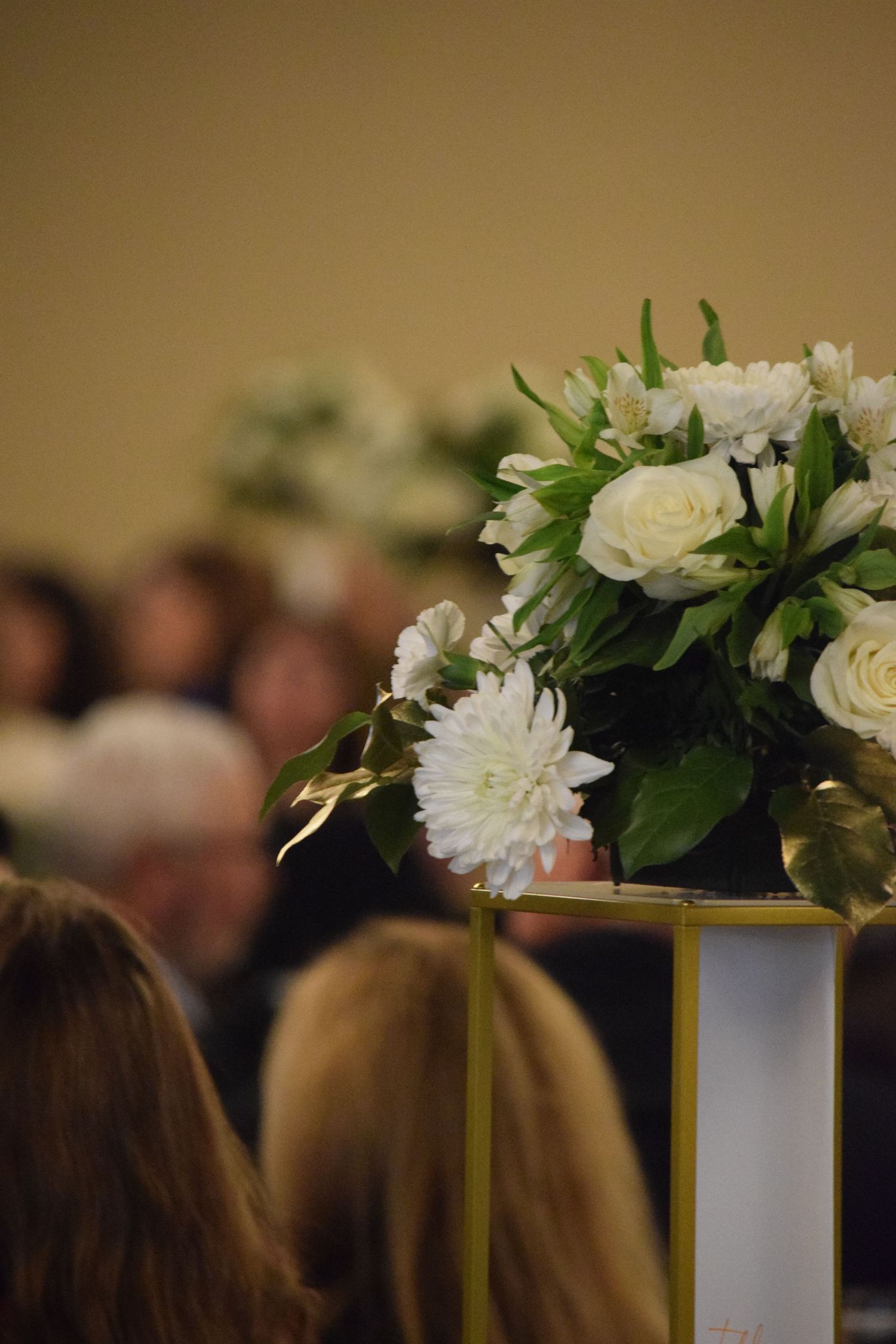 White floral centerpieces with roses and greenery line up on tables at an elegant event venue.