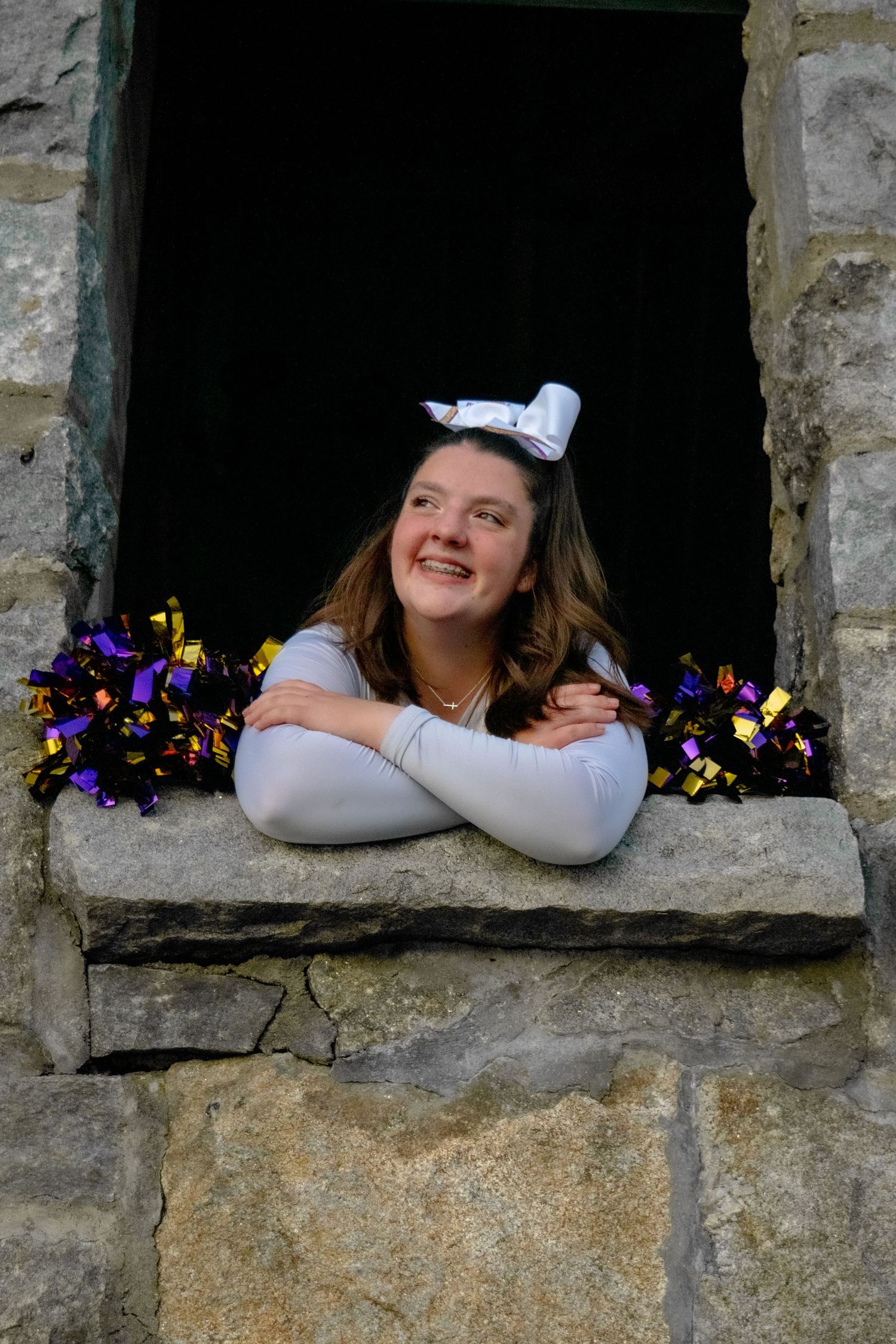 A creative photo series showing someone playfully posing through stone window openings in an old wall with purple flowers.