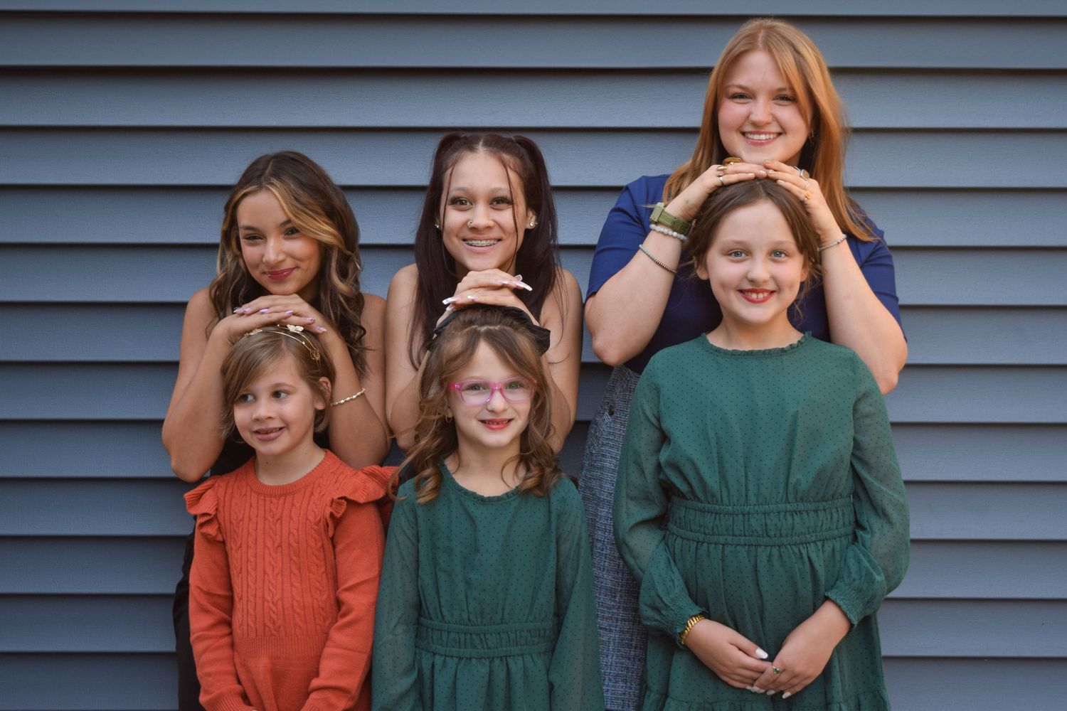 A group of people wearing casual clothing pose together against a blue siding wall.
