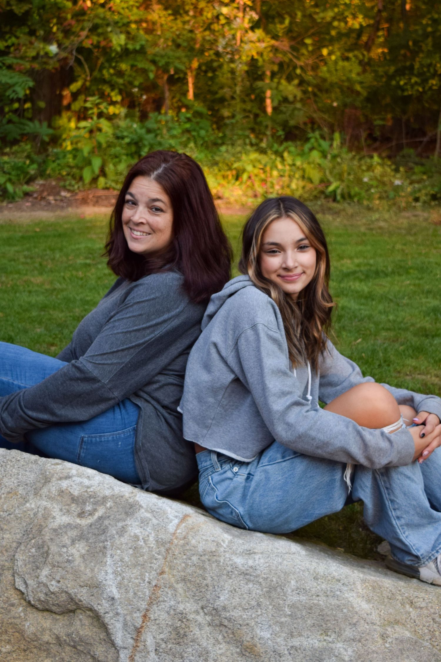 Two people relaxing together on a large rock outdoors during golden hour in casual denim and gray clothing.