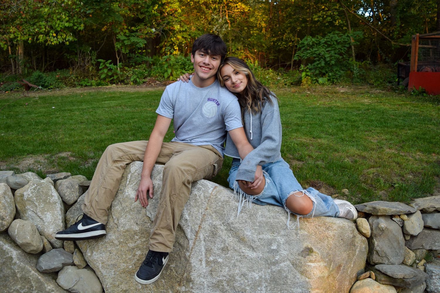A person sits on a stone wall in a backyard garden during autumn with colorful fall foliage in the background.