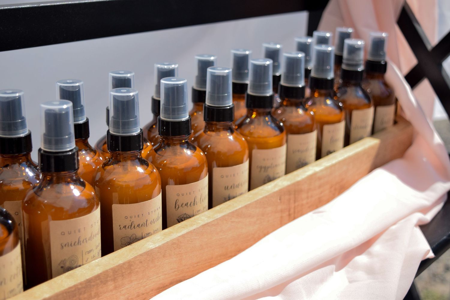Multiple amber glass spray bottles with gray atomizers neatly arranged in a wooden tray display.