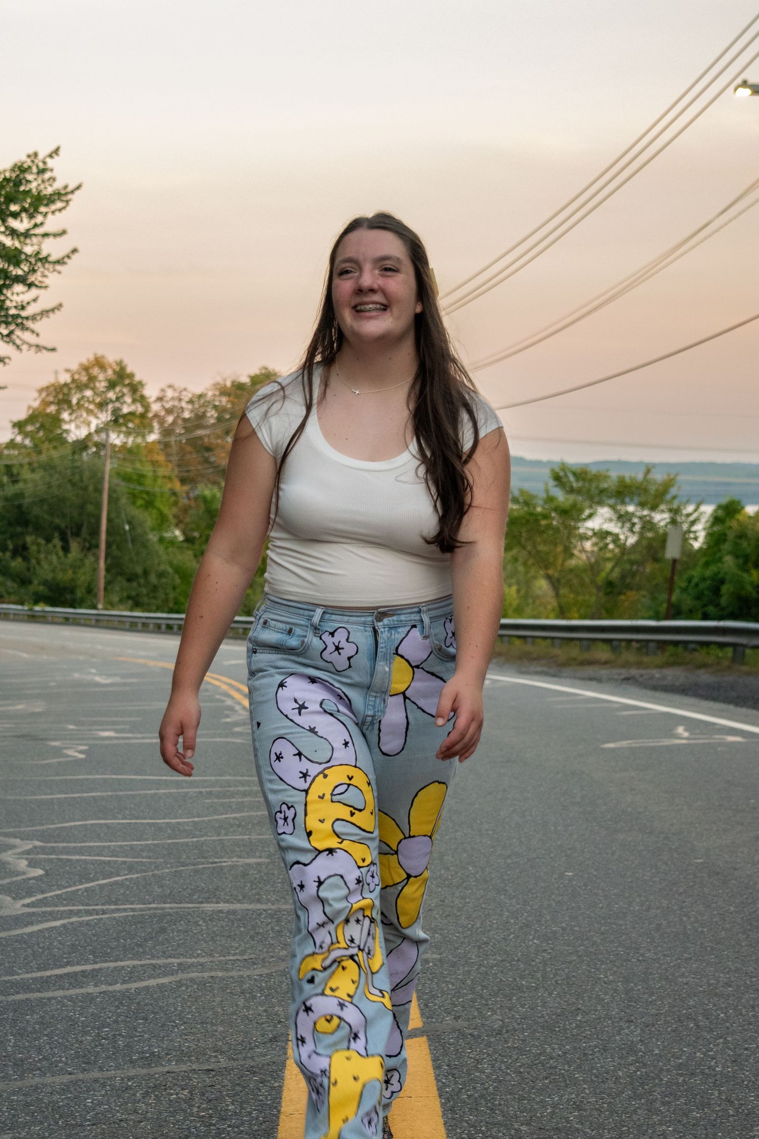 Someone wearing a white tank top and colorful cartoon-patterned leggings stands in an empty parking lot at dusk.