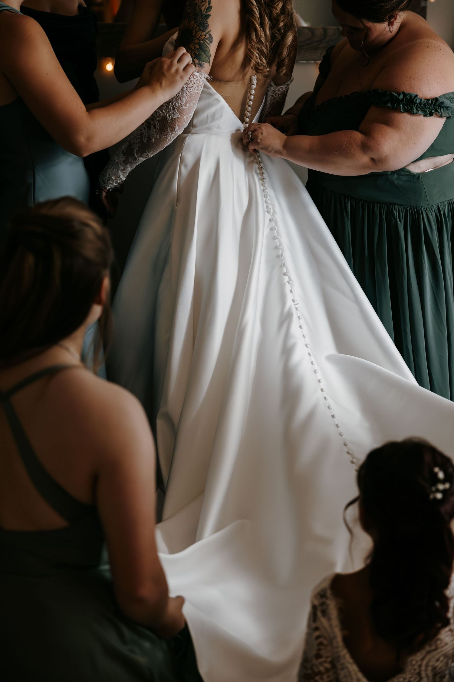 Close-up of bridesmaids helping with the buttons on a white wedding dress.
