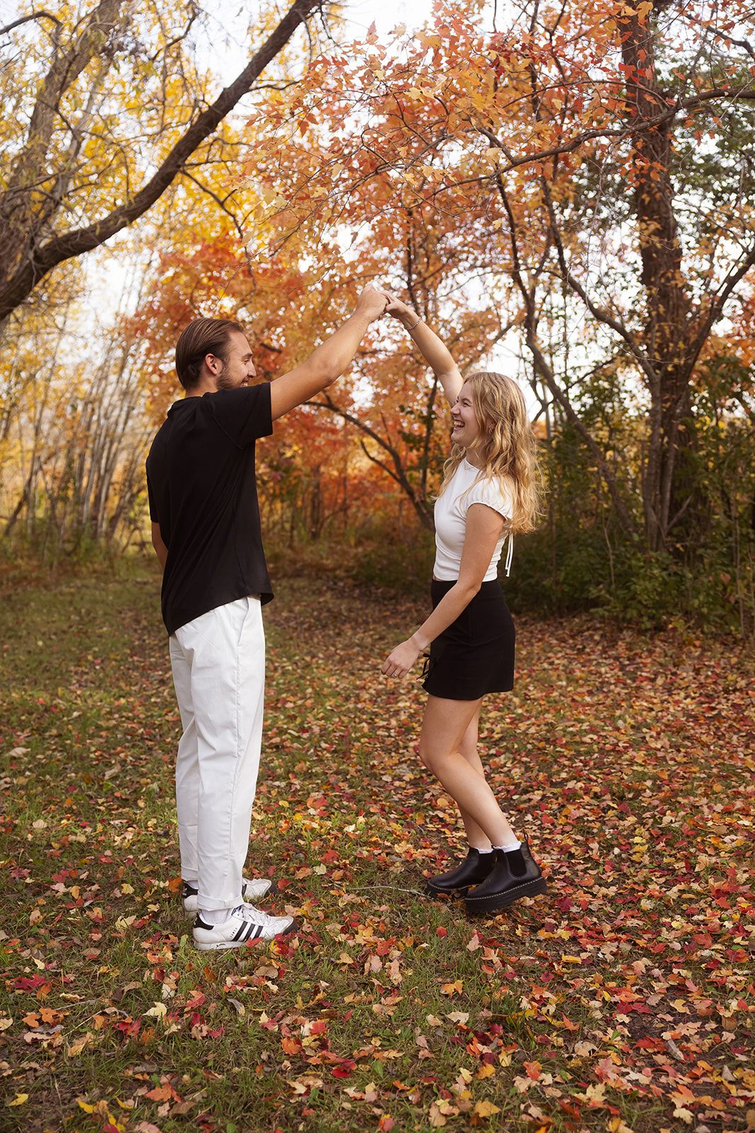 Couple performing dance lifts among fallen autumn leaves in forest setting.