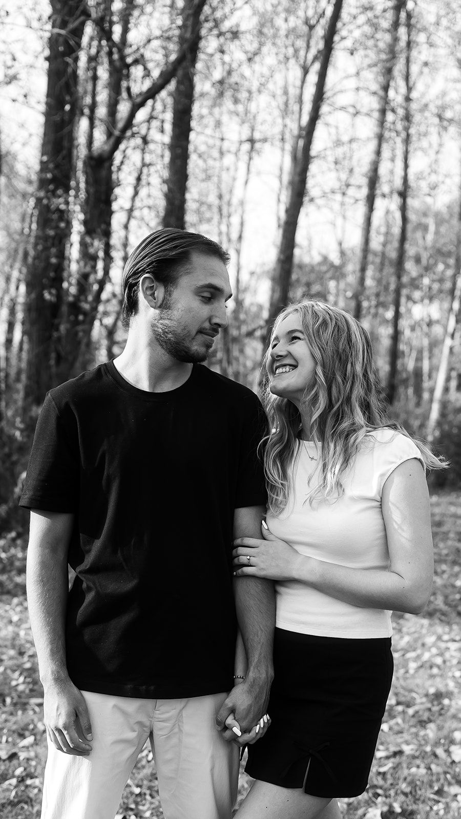 Black and white photo of a couple sharing a candid moment in a forest setting.