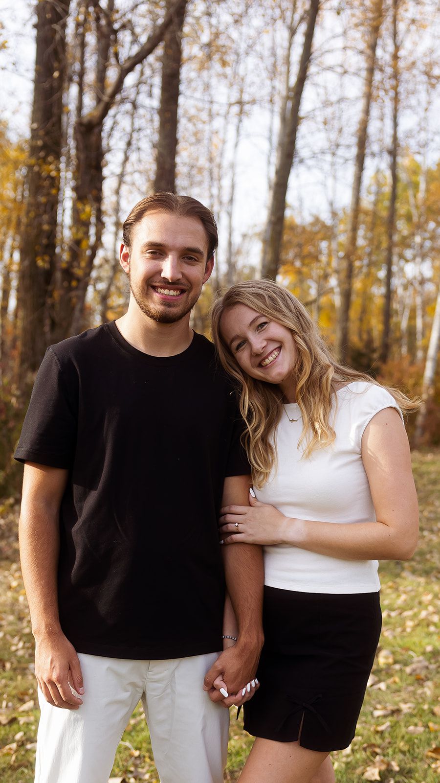 A couple shares joyful laughter while embracing in a wooded setting with fall foliage.